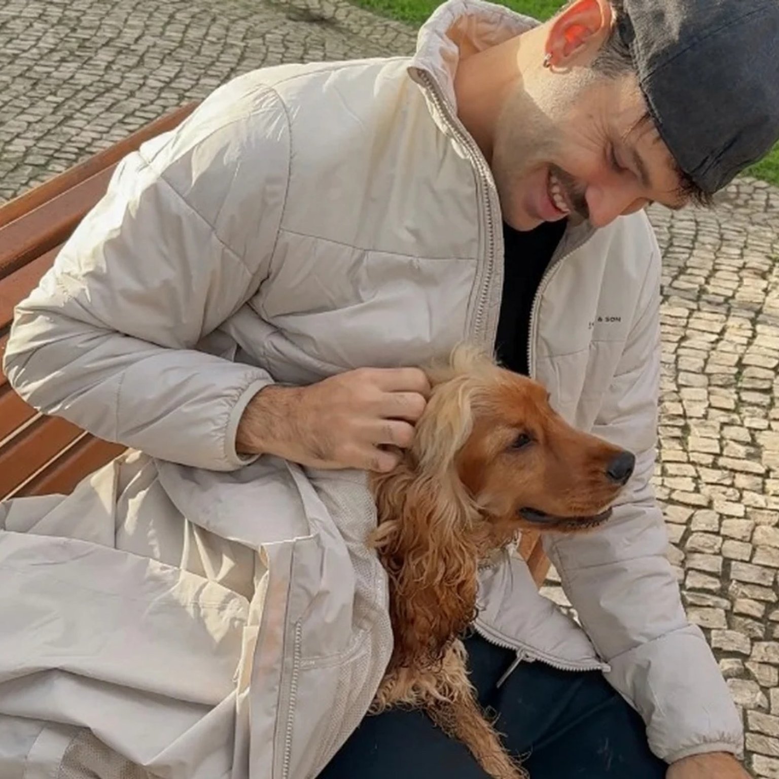 mann streichelt seinen hund und deckt ihn mit seiner kapten & son regenjacke zu