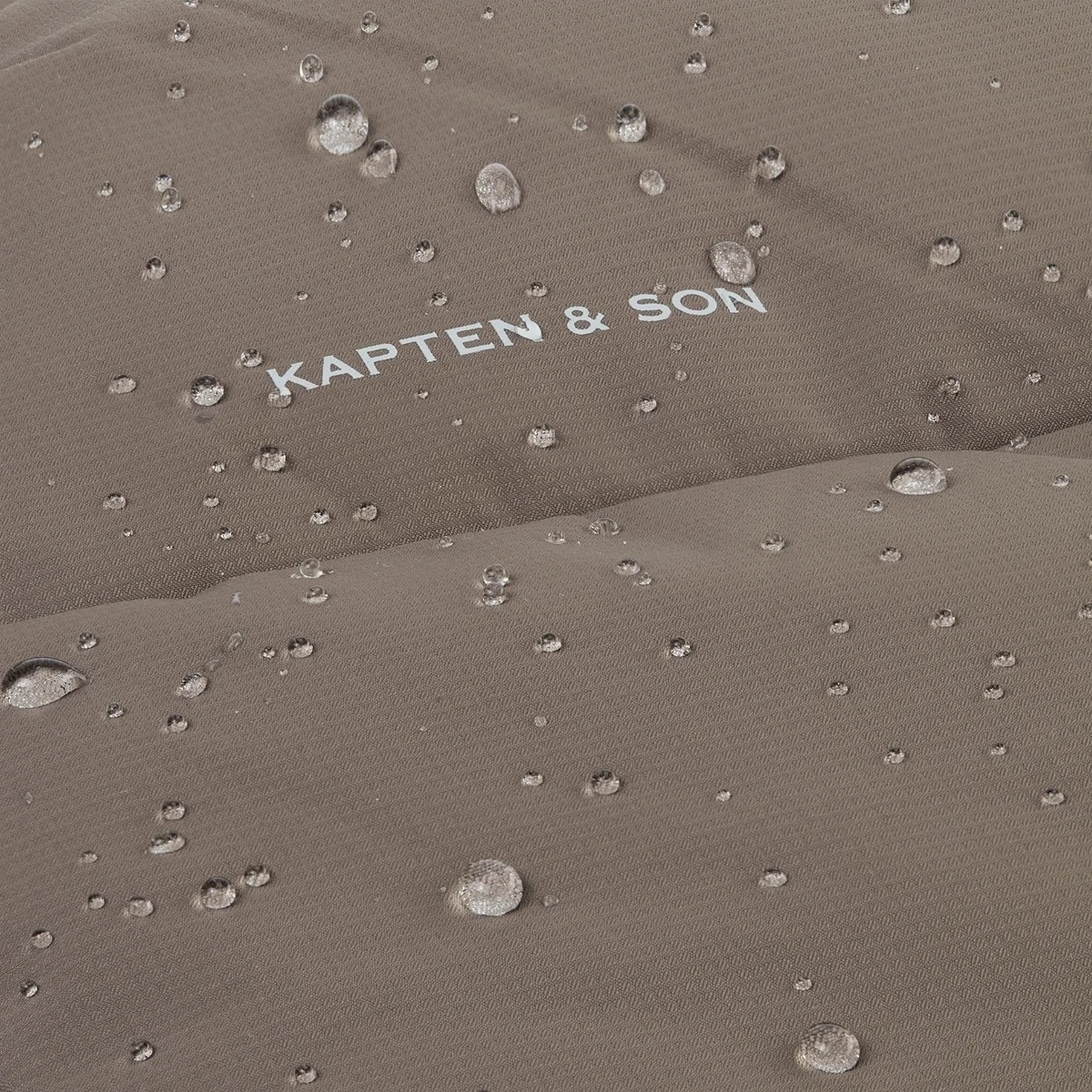 Nahaufnahme von Wassertropfen, die auf dem wasserabweisenden Stoff eines Kleidungsstücks von Kapten & Son abperlen.