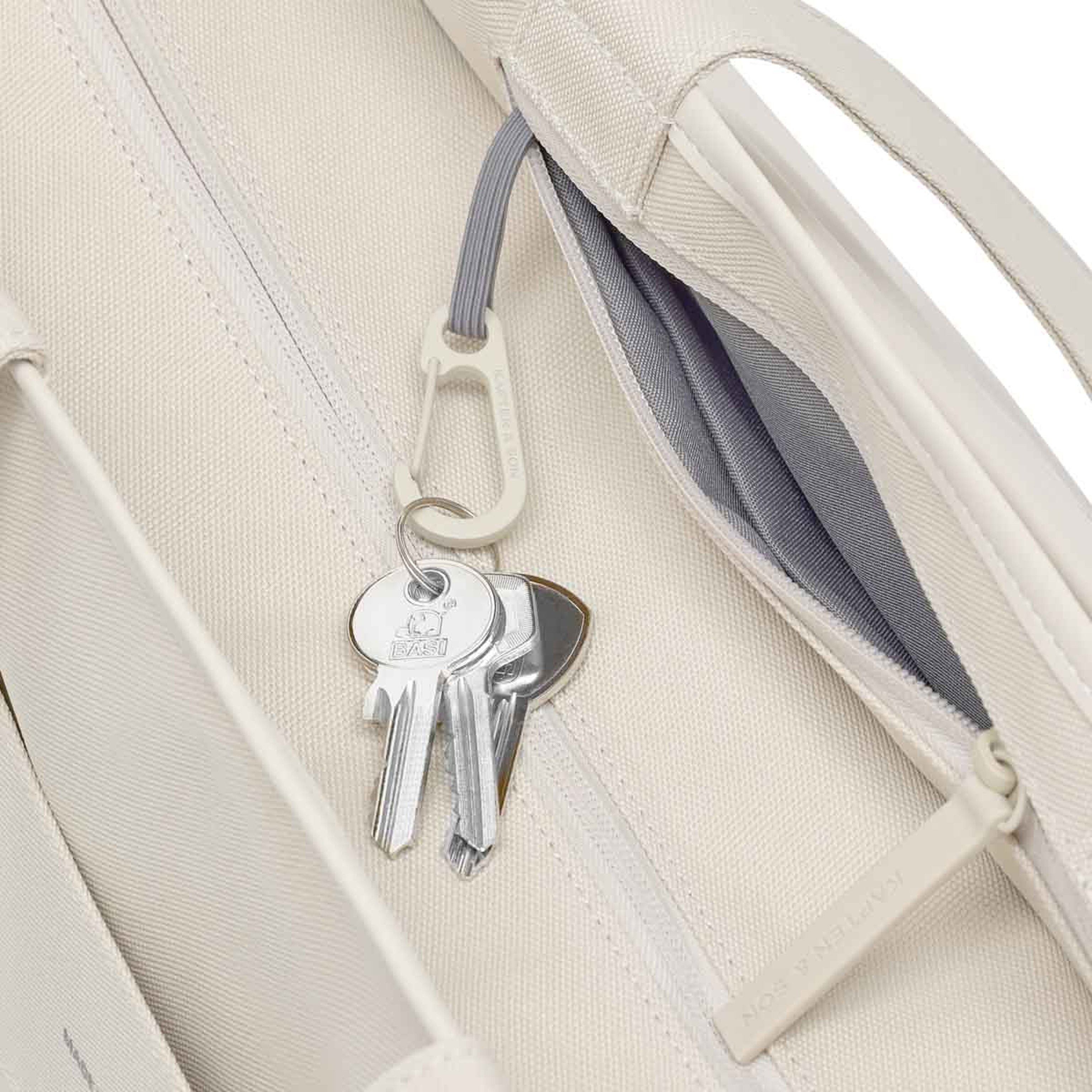 Schlüsselbund an einem kleinen Karabinerhaken im Innenfach einer sandfarbenen Tasche.
