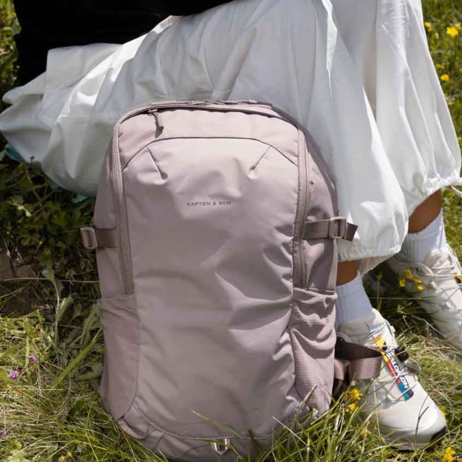 rosa farbener wanderrucksack von kapten and son liegt neben einer wanderin im gras