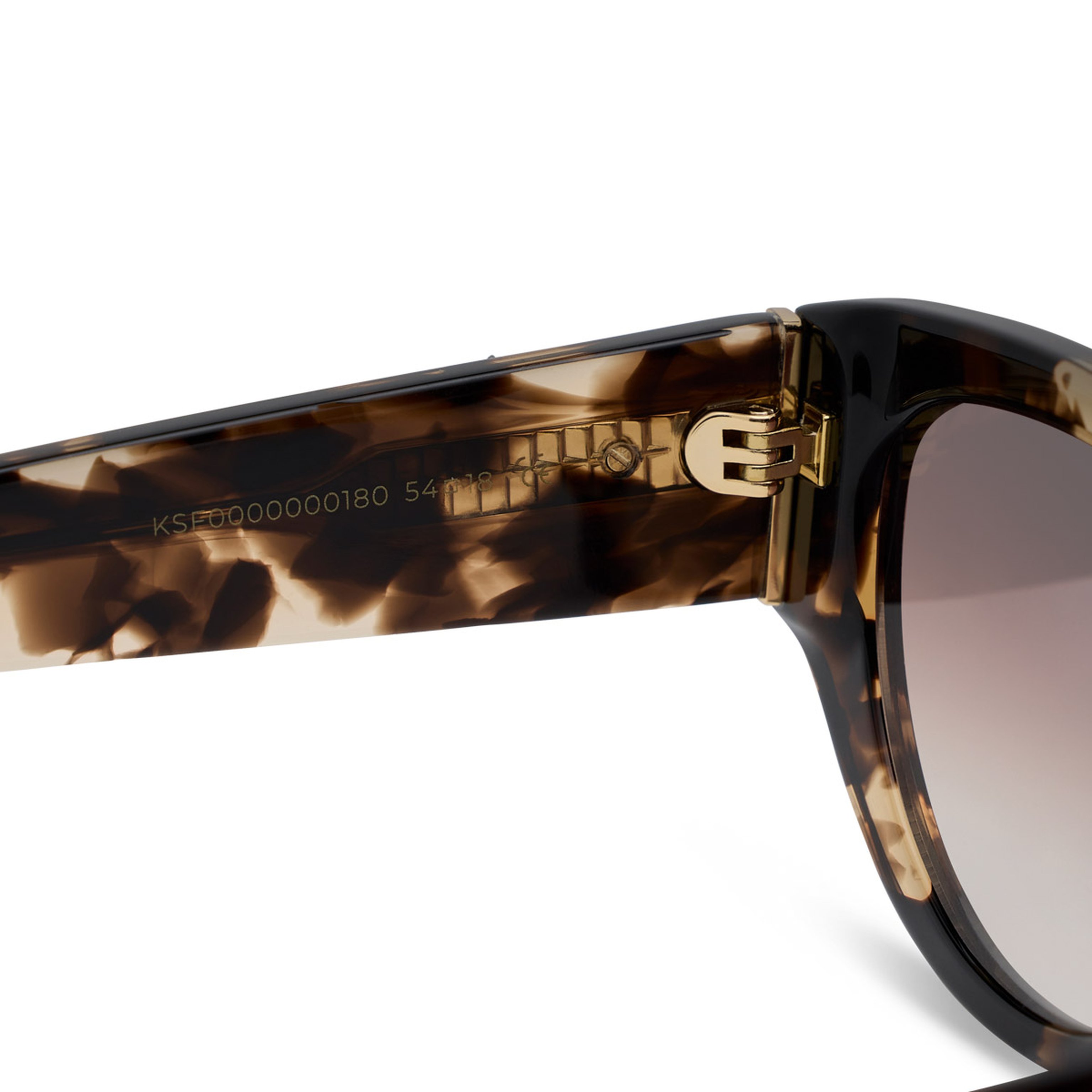 Close-up of tortoiseshell sunglasses showing detailed gold hinge and model number etched on the arm. The design appears modern and stylish.
