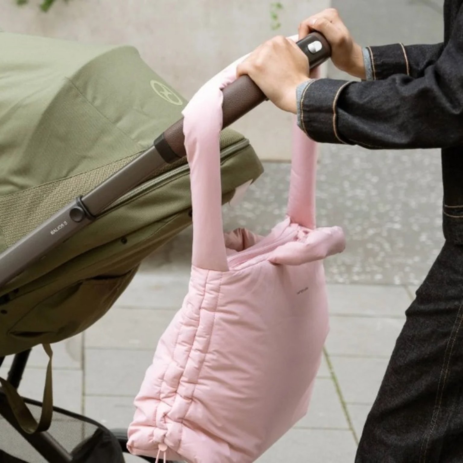 frau schiebt kinderwagen mit rosa wickeltasche dran