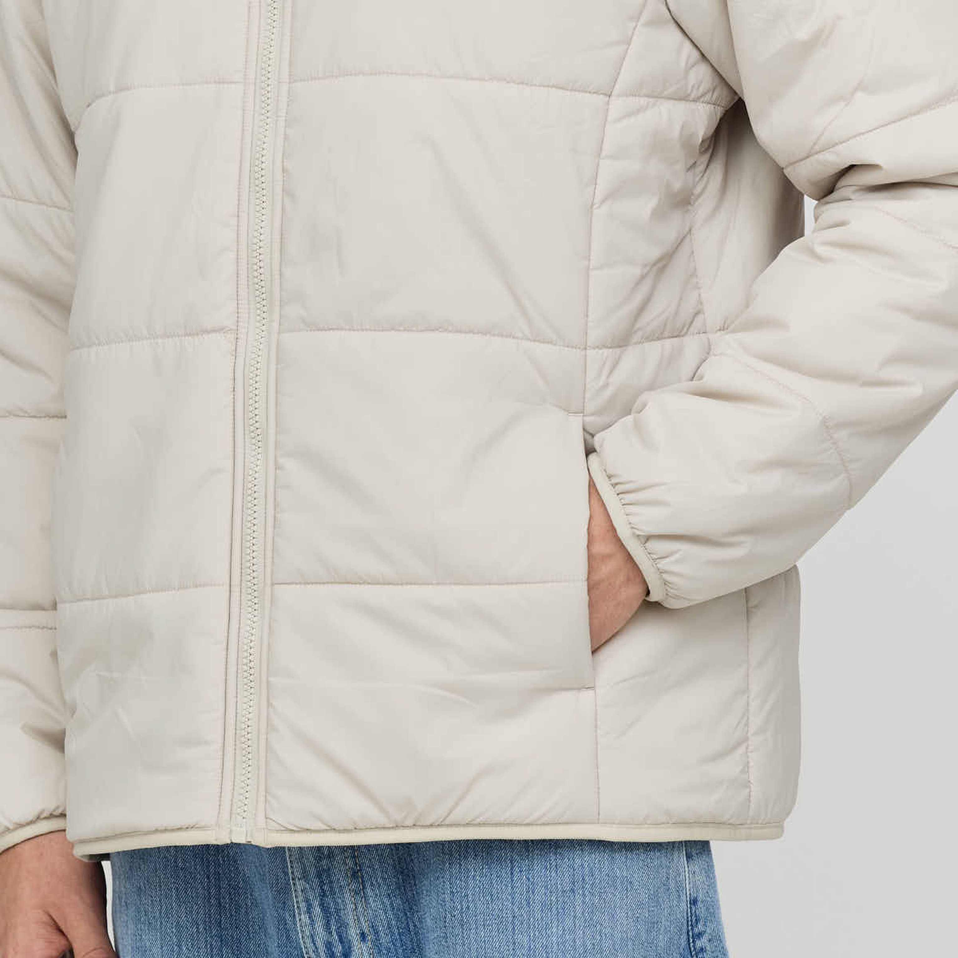 Person wearing a cream-colored, quilted jacket with a visible zipper and hand in pocket, paired with blue jeans. The tone is casual and cozy.