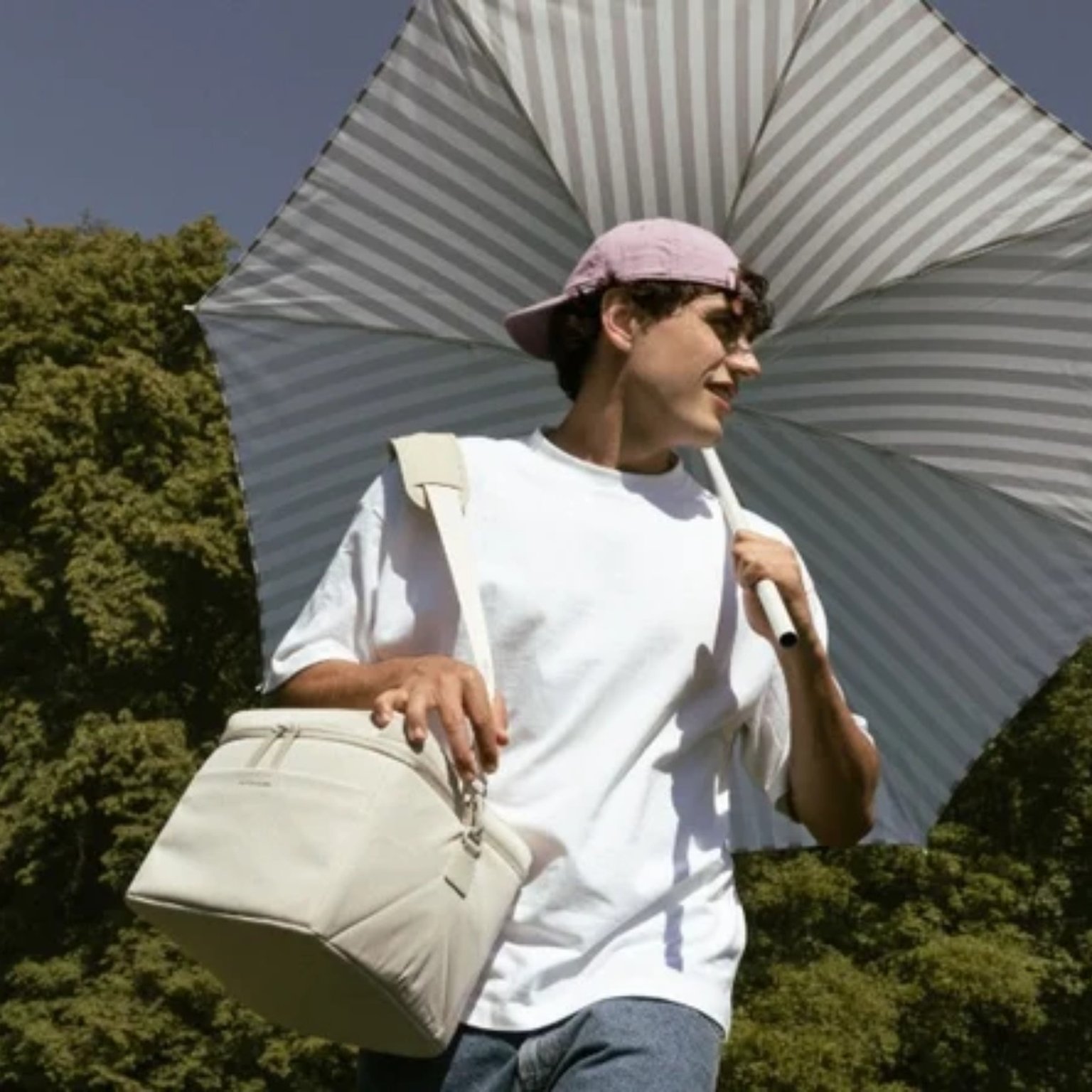 junger mann mit sonnenschirm trägt eine kapten son picknicktasche