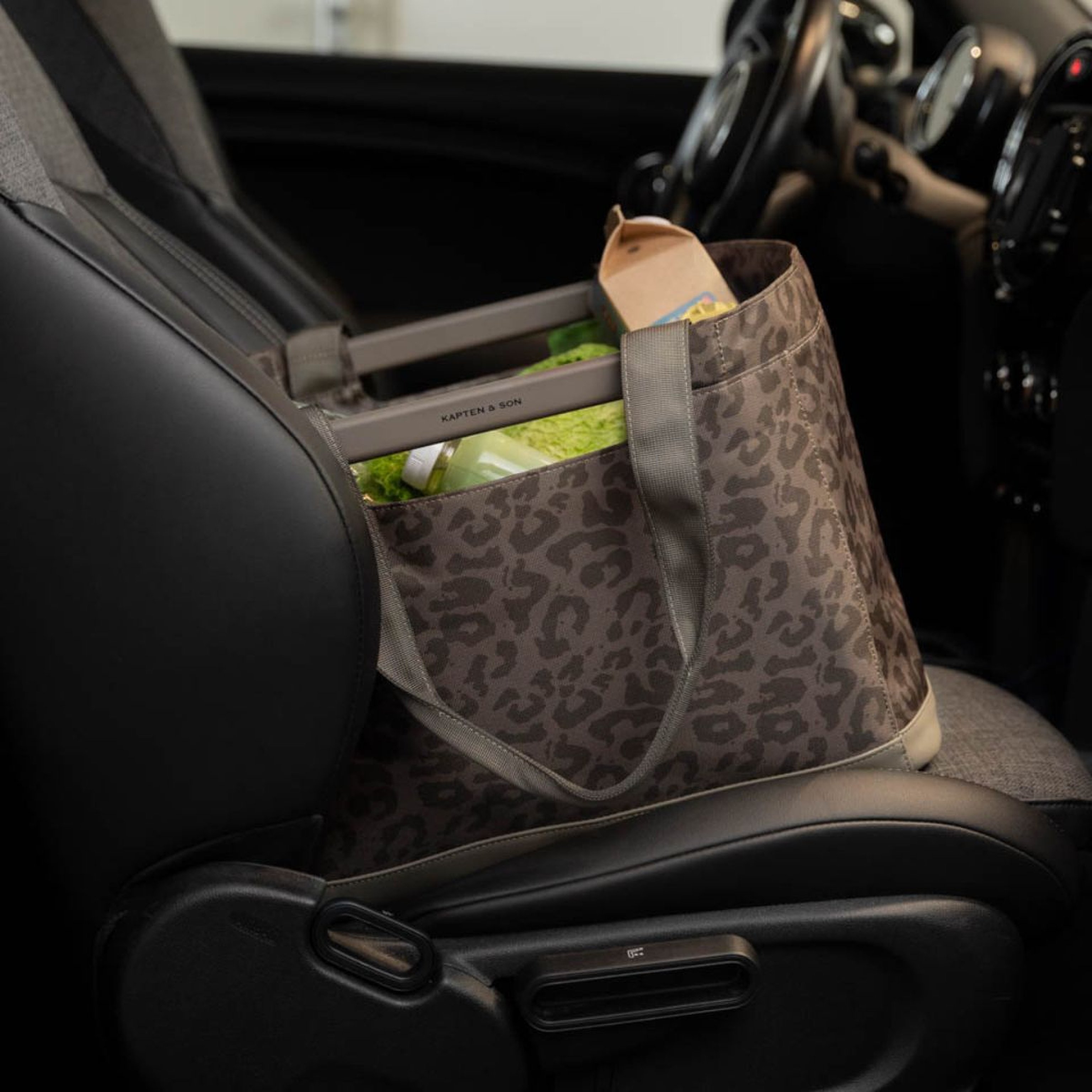 A shopping basket filled with groceries, including baguettes and a cabbage, placed on the front seat of a car. The scene conveys convenience and freshness.