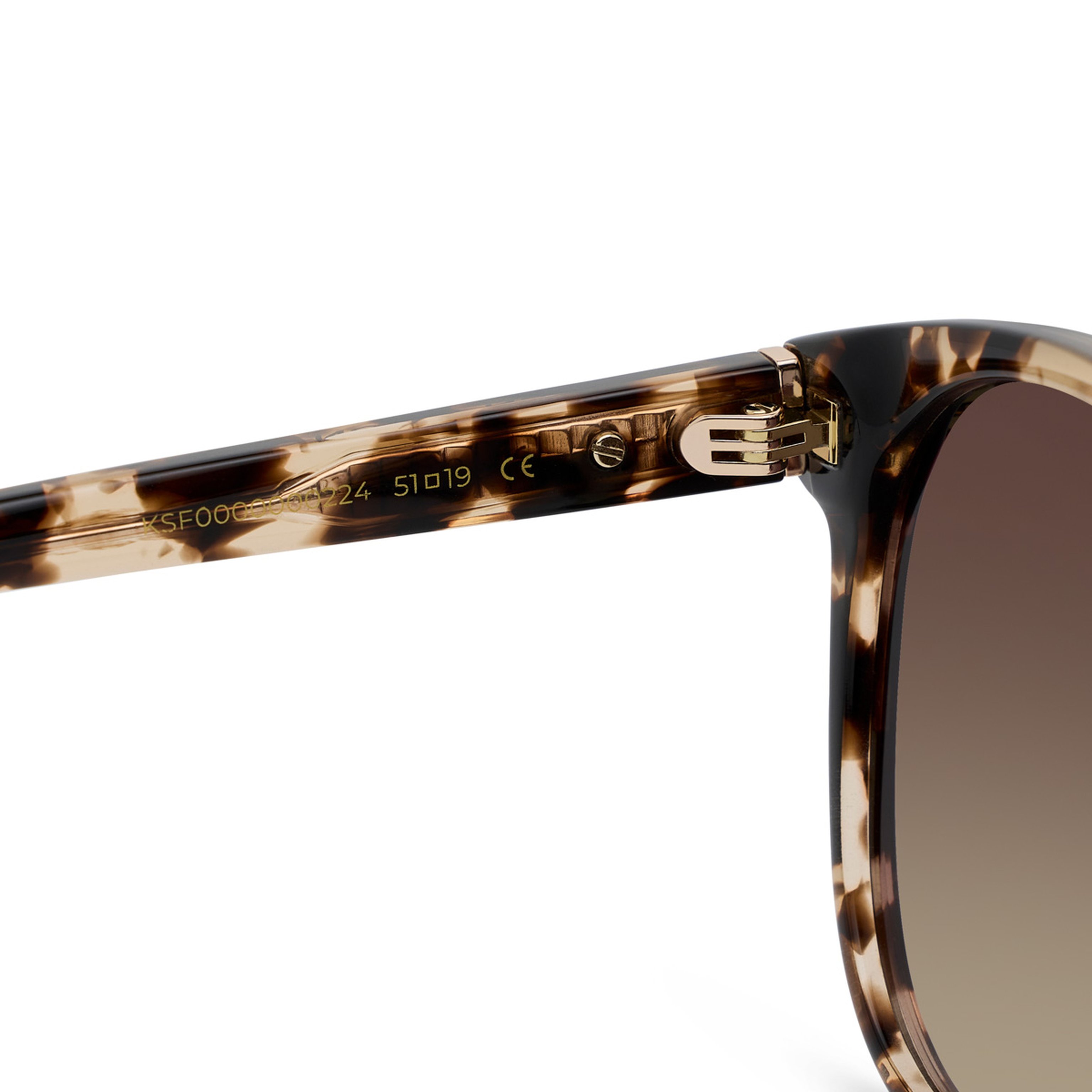 Close-up of tortoiseshell sunglasses showing detailed gold hinge and model number etched on the arm. The design appears modern and stylish.