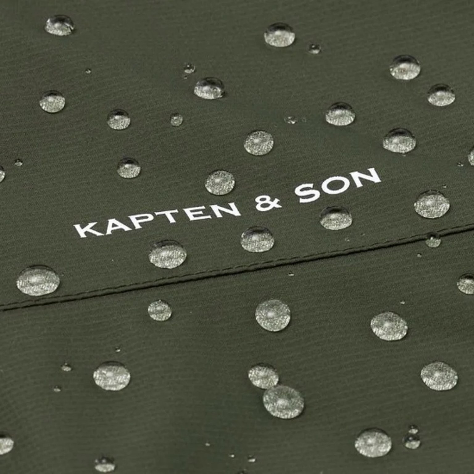 nahaufnahme von regentropfen, die auf einer grünen kapten & son regenjacke abbrallen