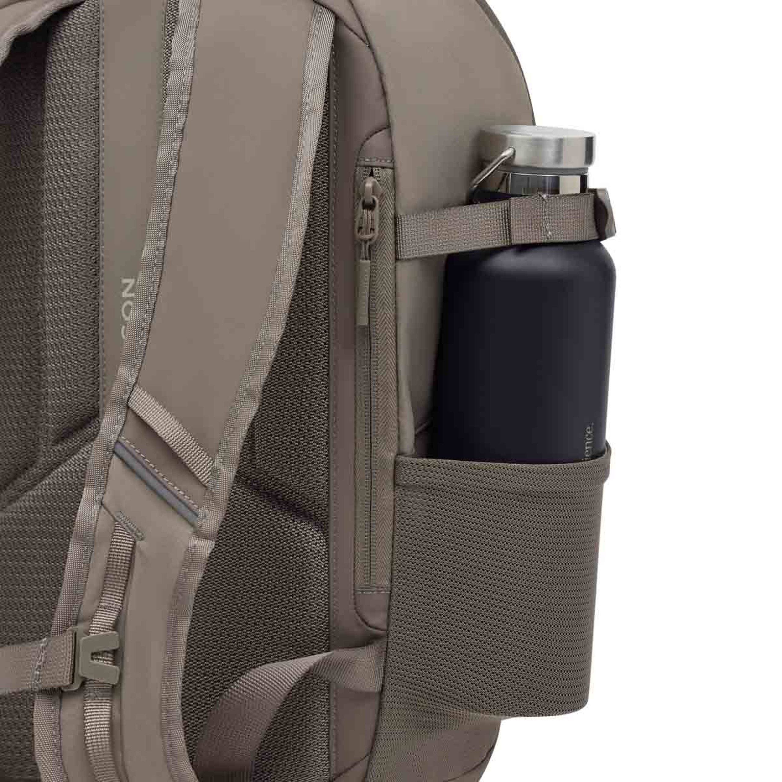 Nahaufnahme der Seite eines beigefarbenen Rucksacks mit einer dunkelnavyblauen Wasserflasche in der Mesh-Seitentasche. Eine seitliche Reißverschlusstasche sowie der gepolsterte Schulterriemen mit dem Kapten & Son Logo sind zu sehen, zusammen mit weiteren Gurten und Schnallen.