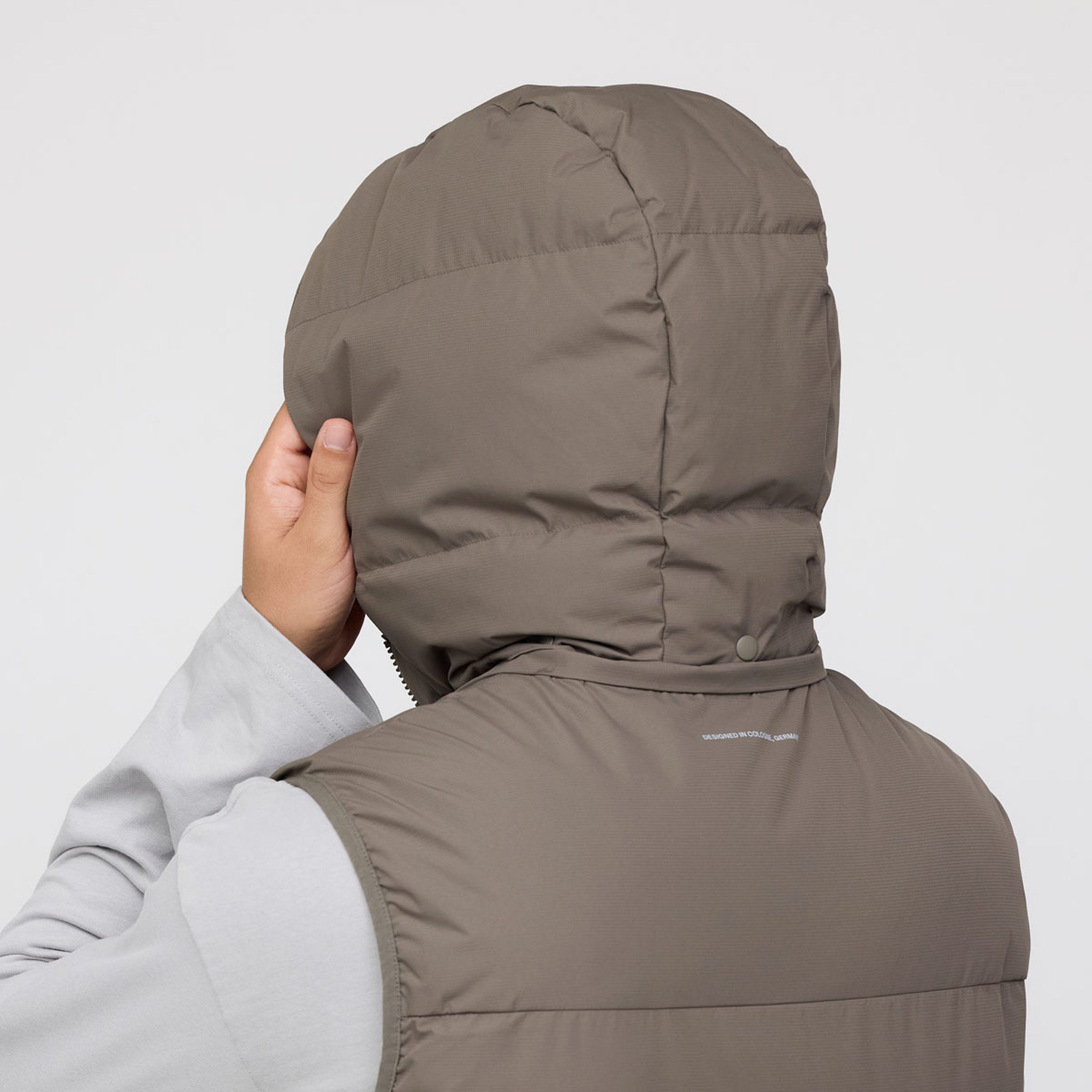 Nahaufnahme einer von hinten sichtbaren Person mit einer wattierten Weste mit Kapuze, die mit einer Hand die Kapuze richtet.