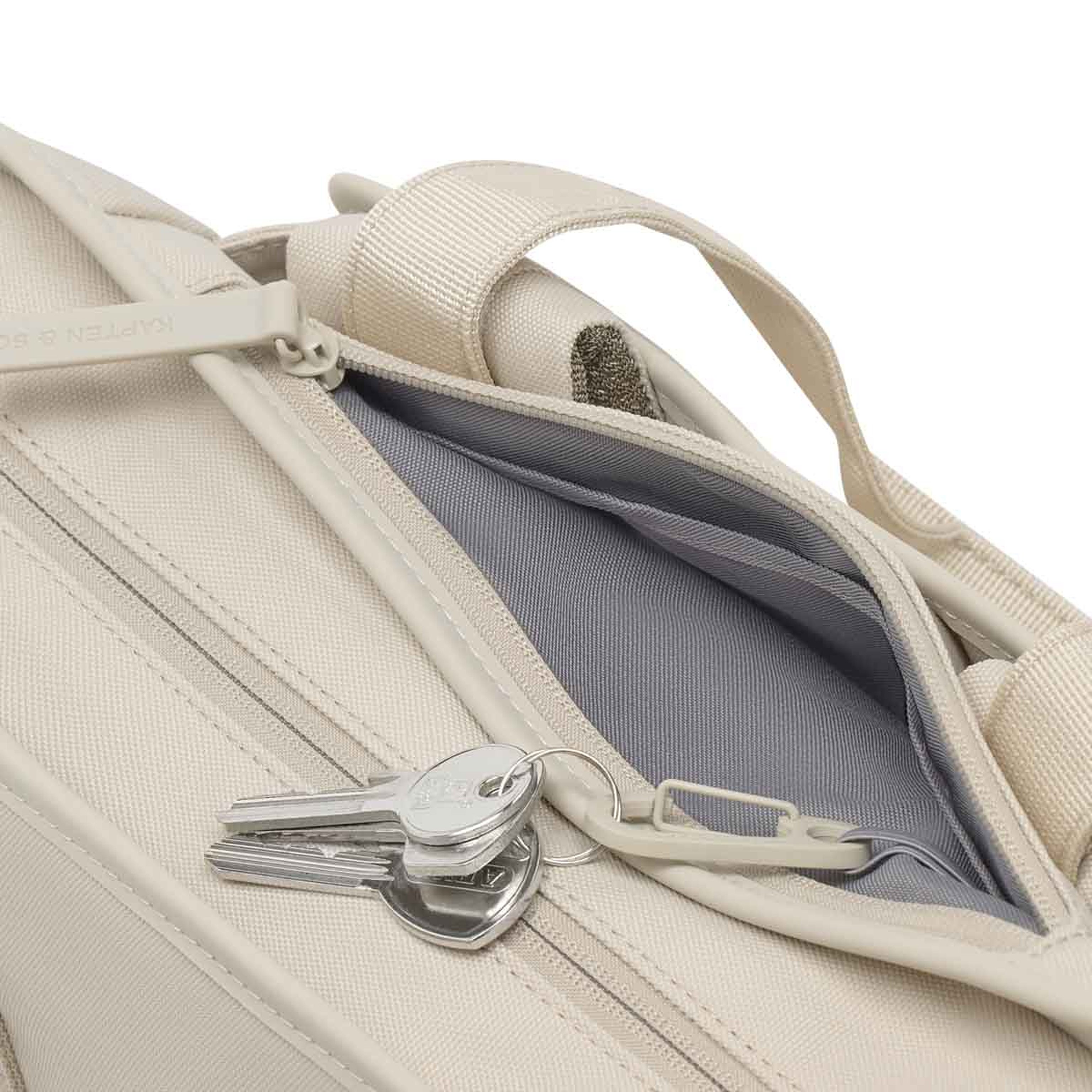 Schlüsselbund an einem kleinen Karabinerhaken im Innenfach einer sandfarbenen Tasche.