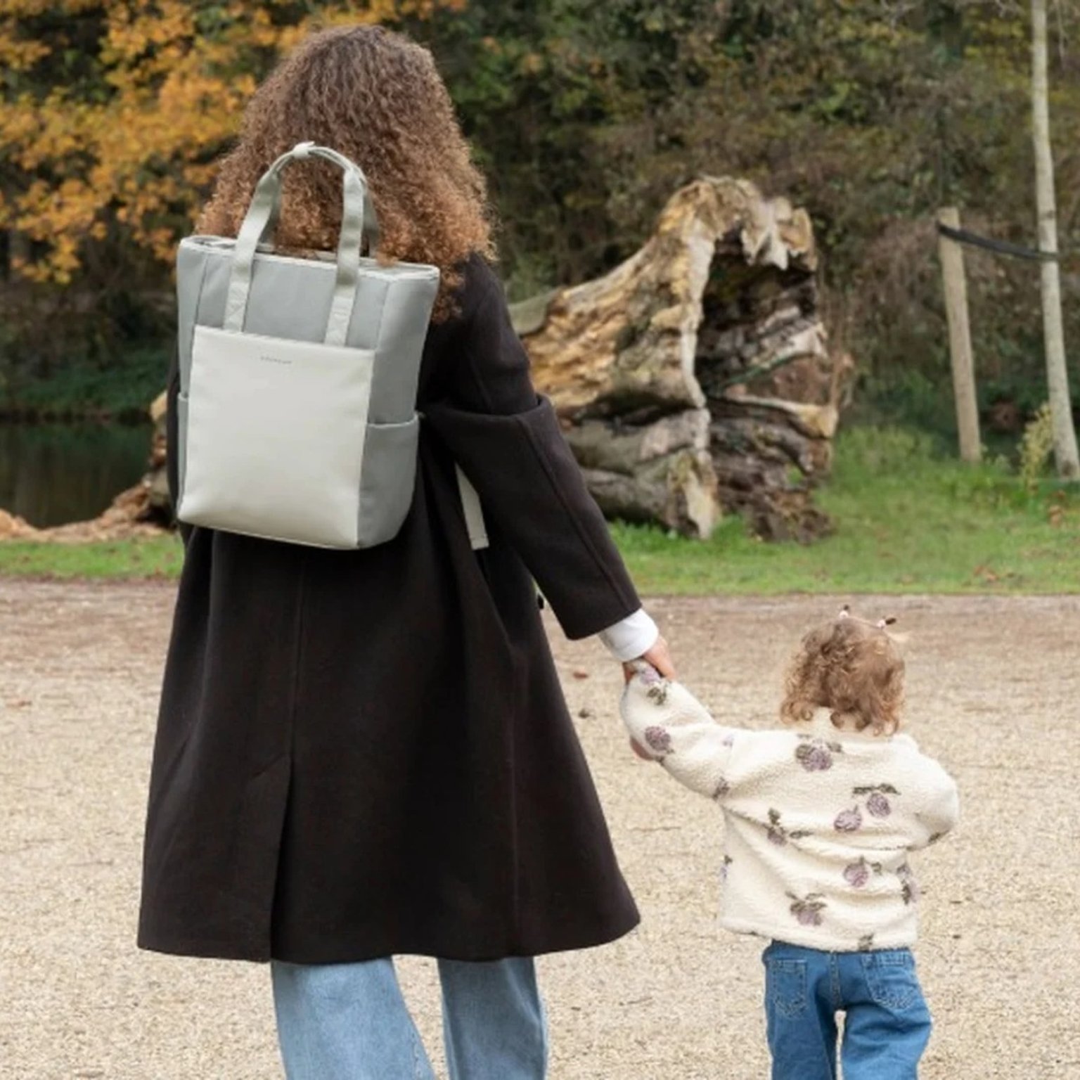 junge mama mit kapten son wickelrucksack geht mit ihrer tochter an der hand spazieren