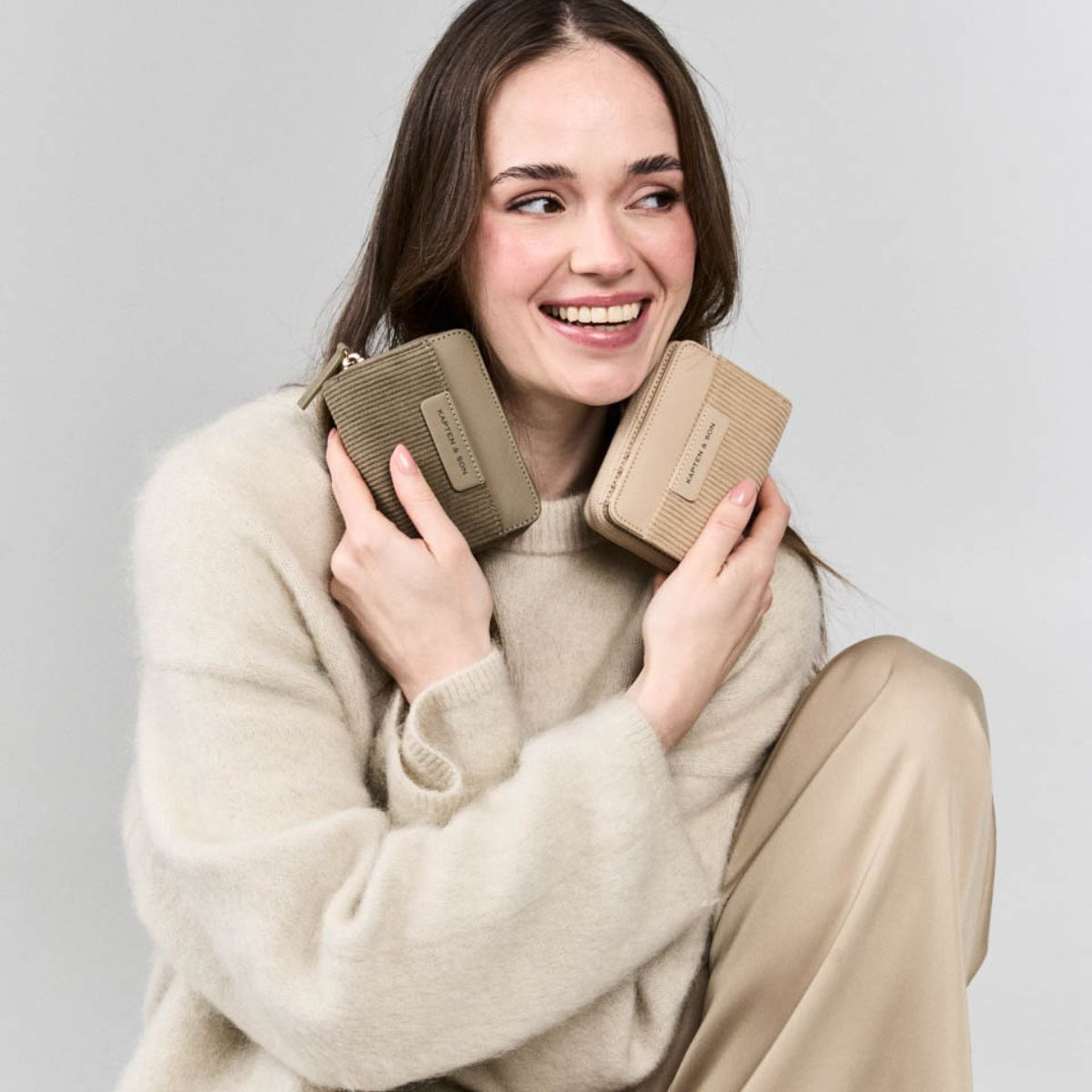 Eine Frau in einem gemütlichen Pullover hält zwei Geldbörsen in der Hand und lächelt sanft, während sie für das Foto posiert.