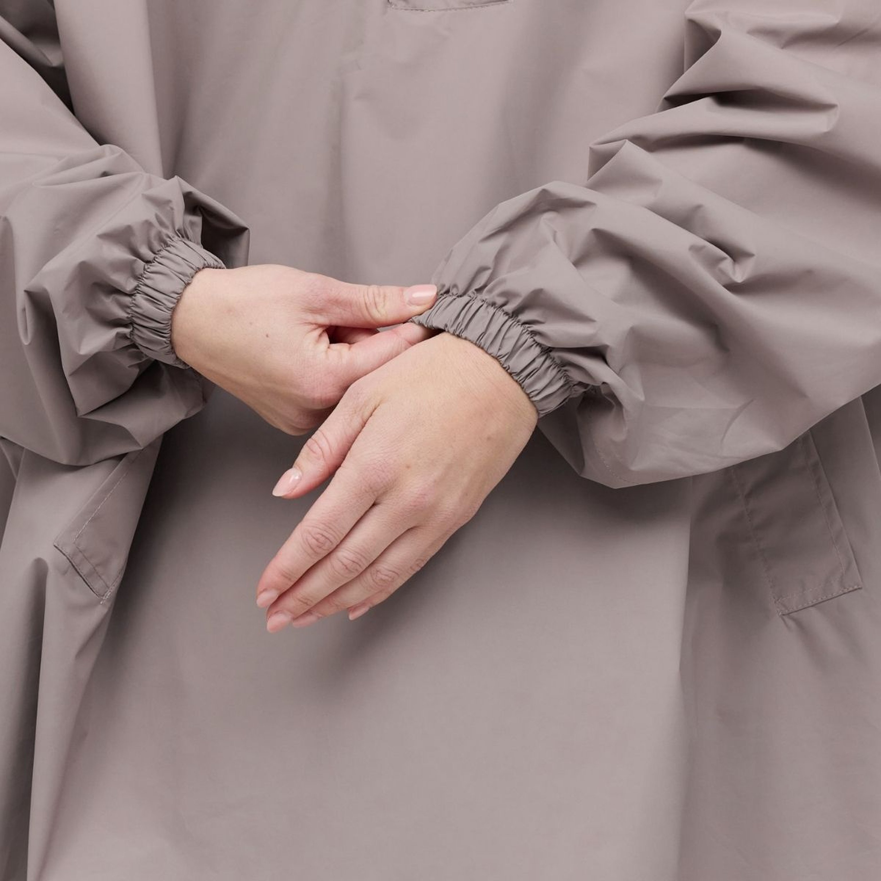 Hands adjust the elastic cuff of a rain jacket. The fabric appears smooth and slightly oversized, conveying a sense of calm and comfort.