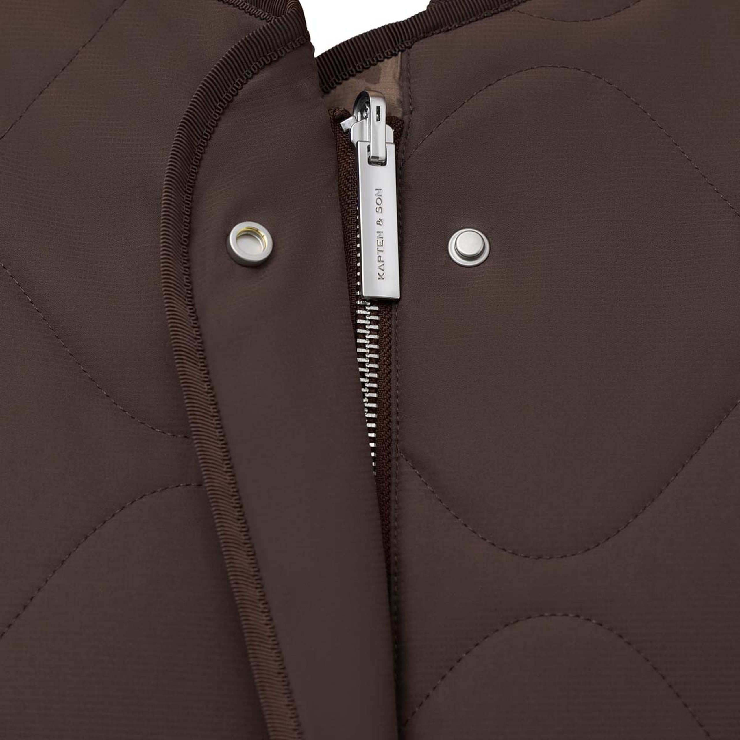 Nahaufnahme der gesteppten Jacke mit Frontreißverschluss und Zipper mit Markenlogo