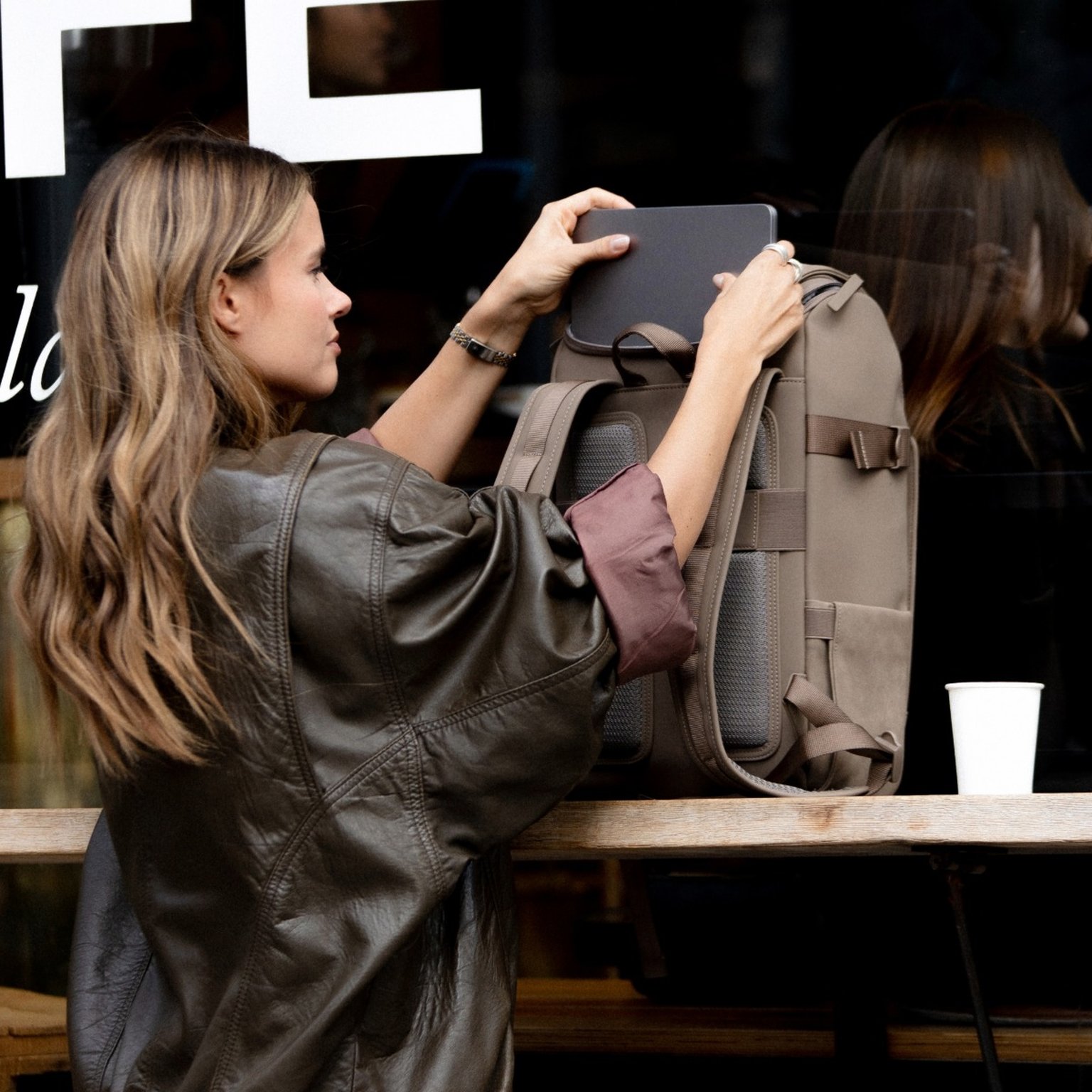 frau sitzt vor einem café und zieht ihren laptop aus einem rucksack 