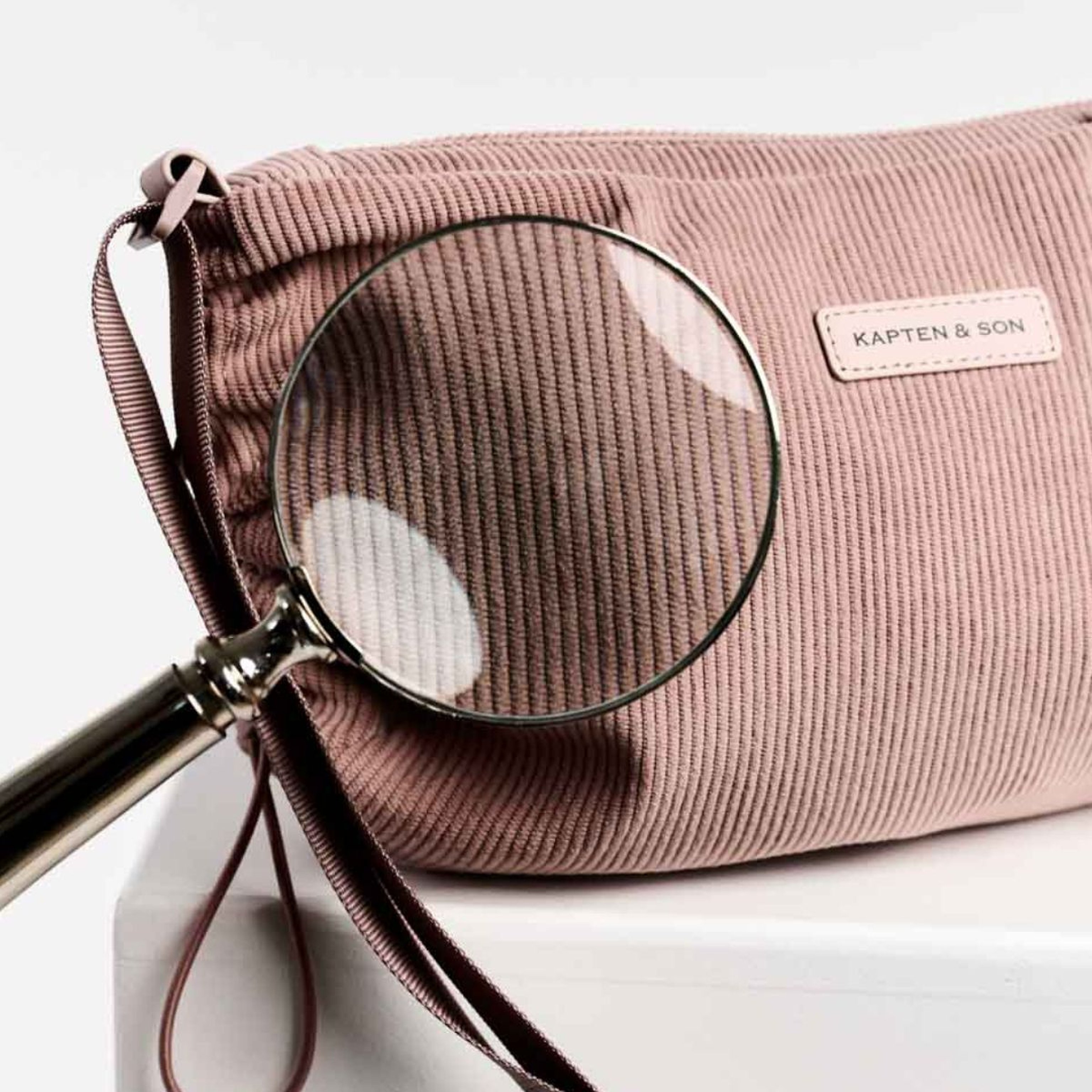 Un bolso rosa con una lupa encima, que muestra una combinación de accesorios elegante y curiosa.