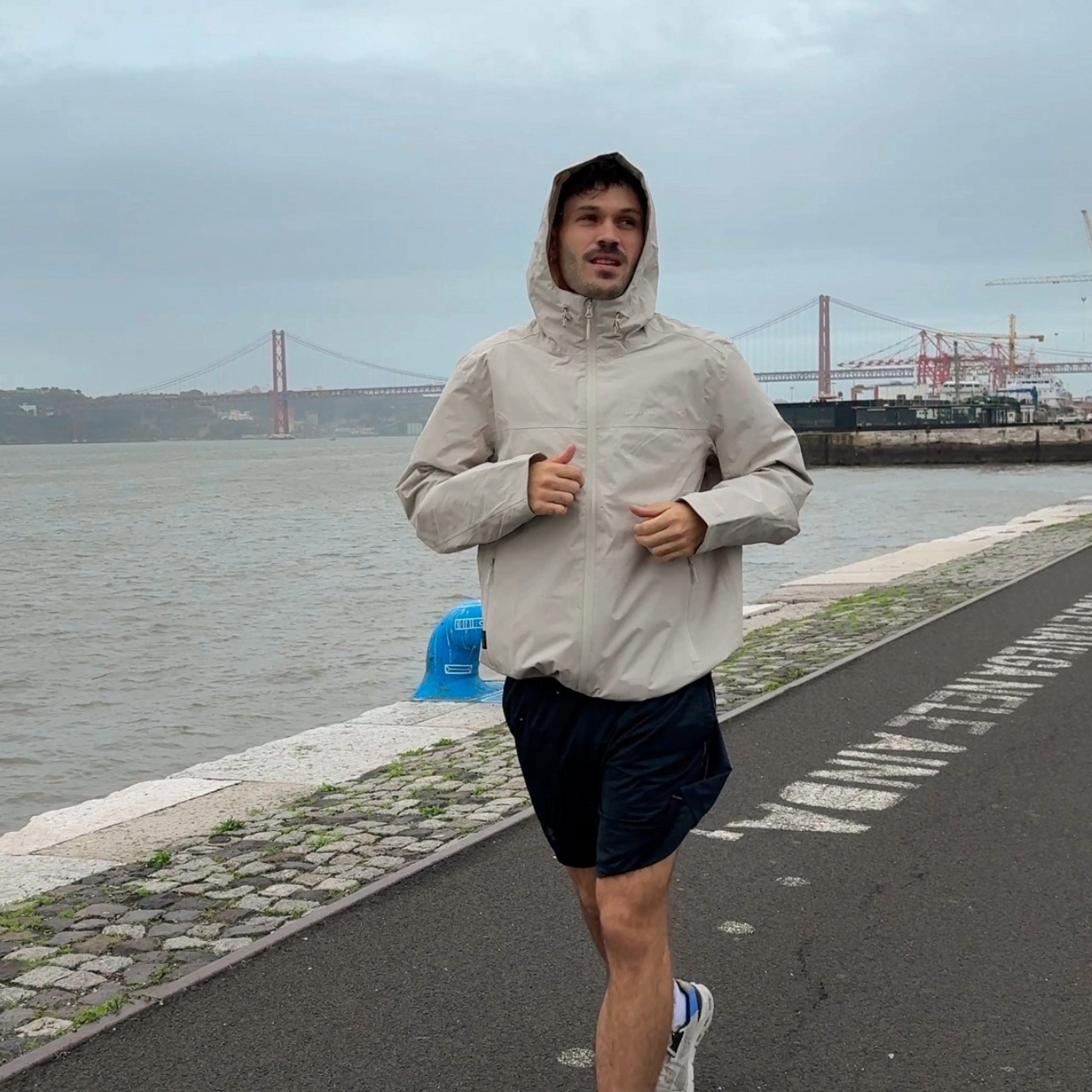 junger mann joggt mit heller laufjacke am wasser 