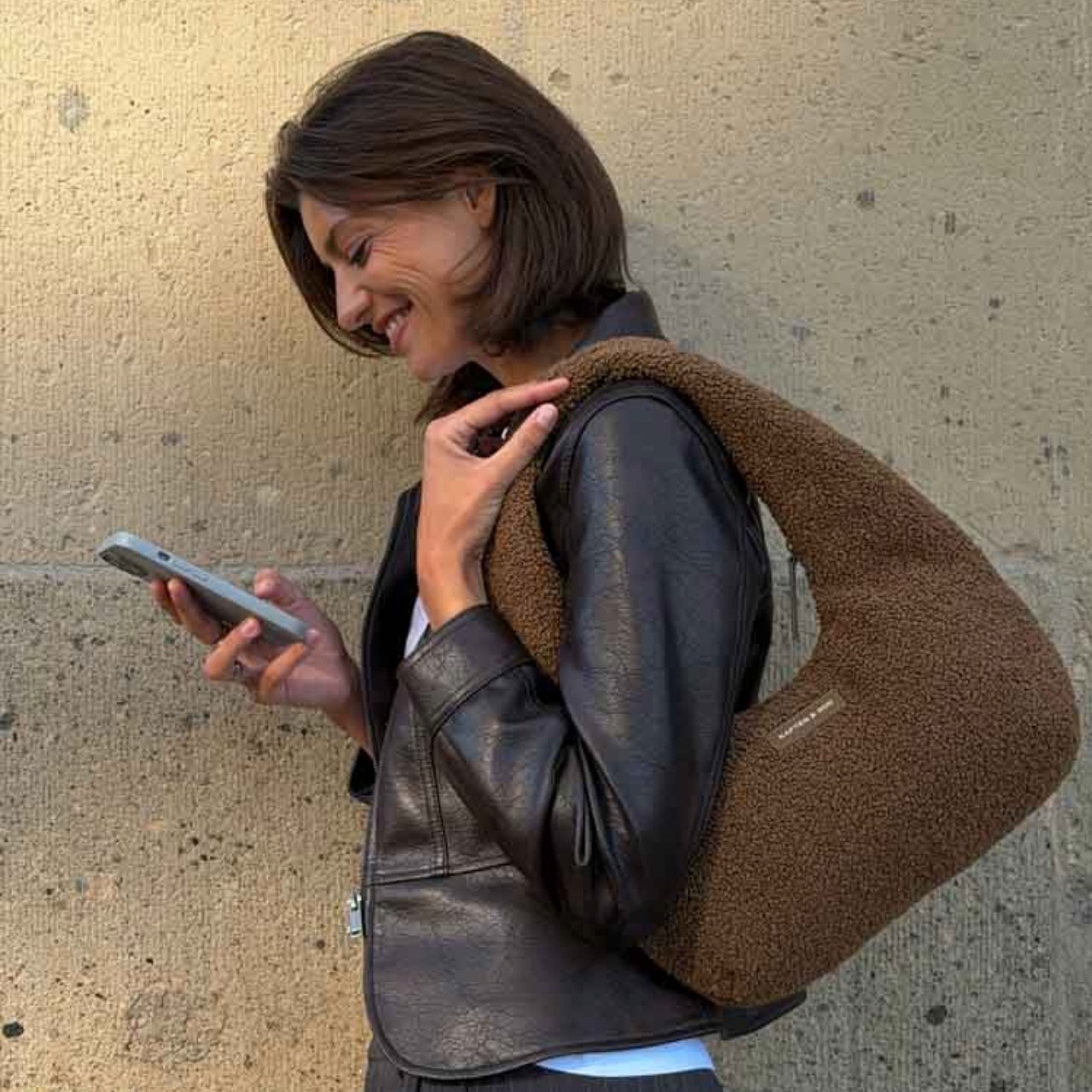 Frau schaut aufs handy und trägt eine braune kapten & son fleece tasche