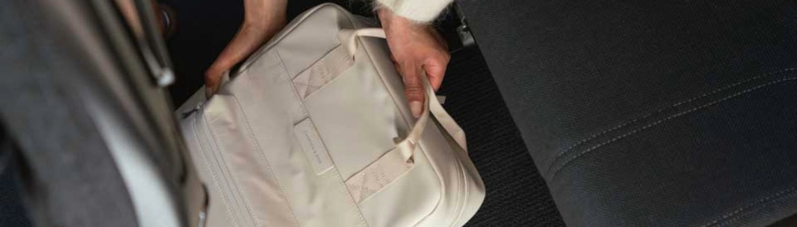 frau führt 40 x 30 x 20 cm großen hellen rucksack unter den flugzeug sitz ein