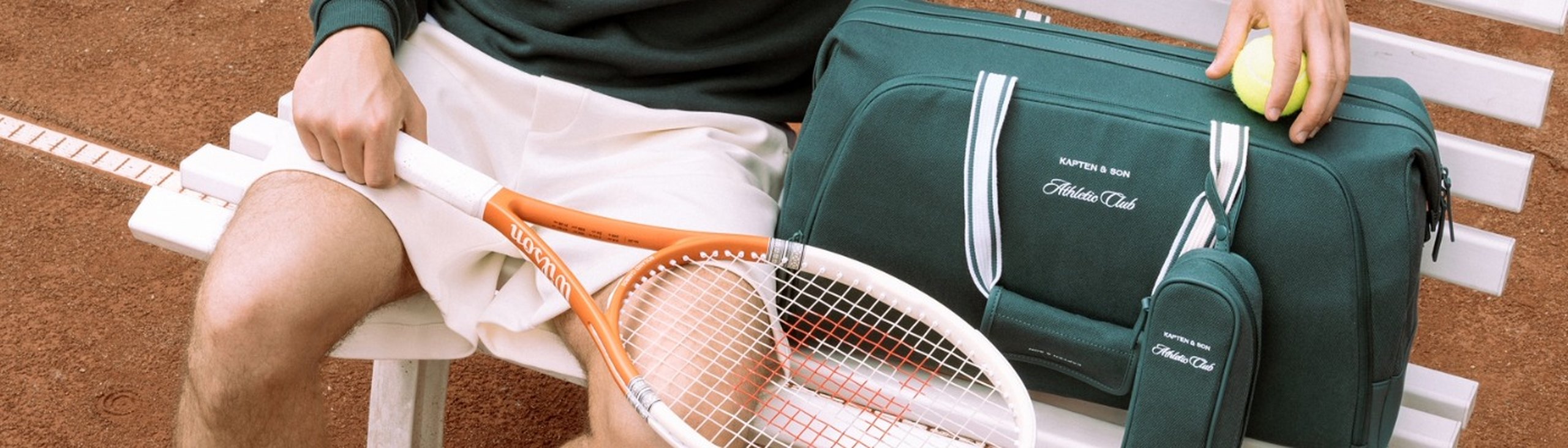 Mann sitzt mit tennisschläger und kapten and son sporttasche auf einer bank