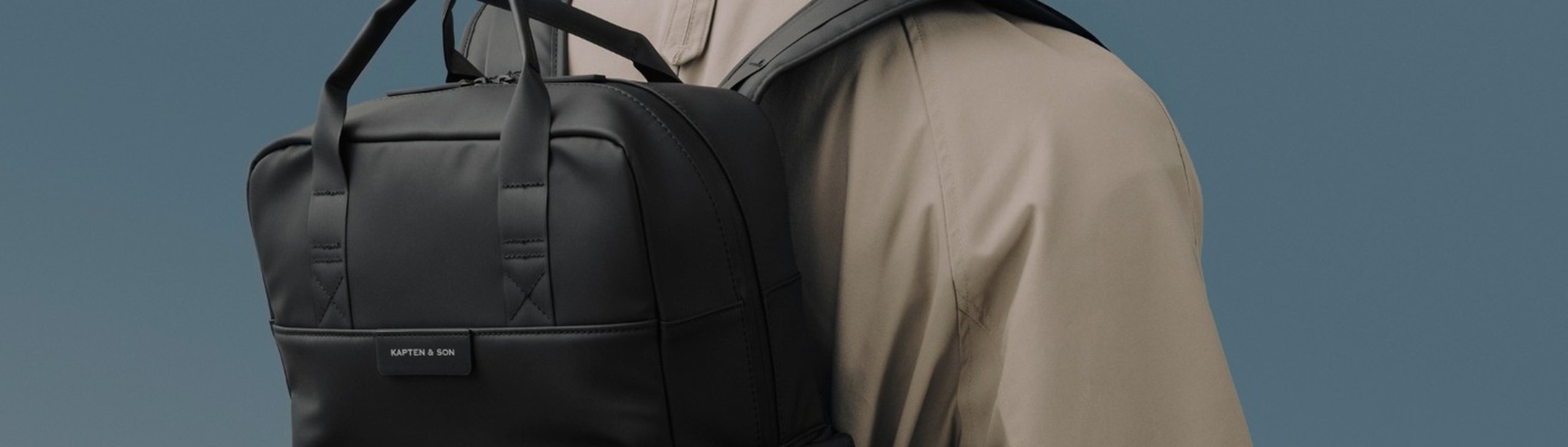 man im trenchcoat trägt schwarzen business rucksack von kapten and son