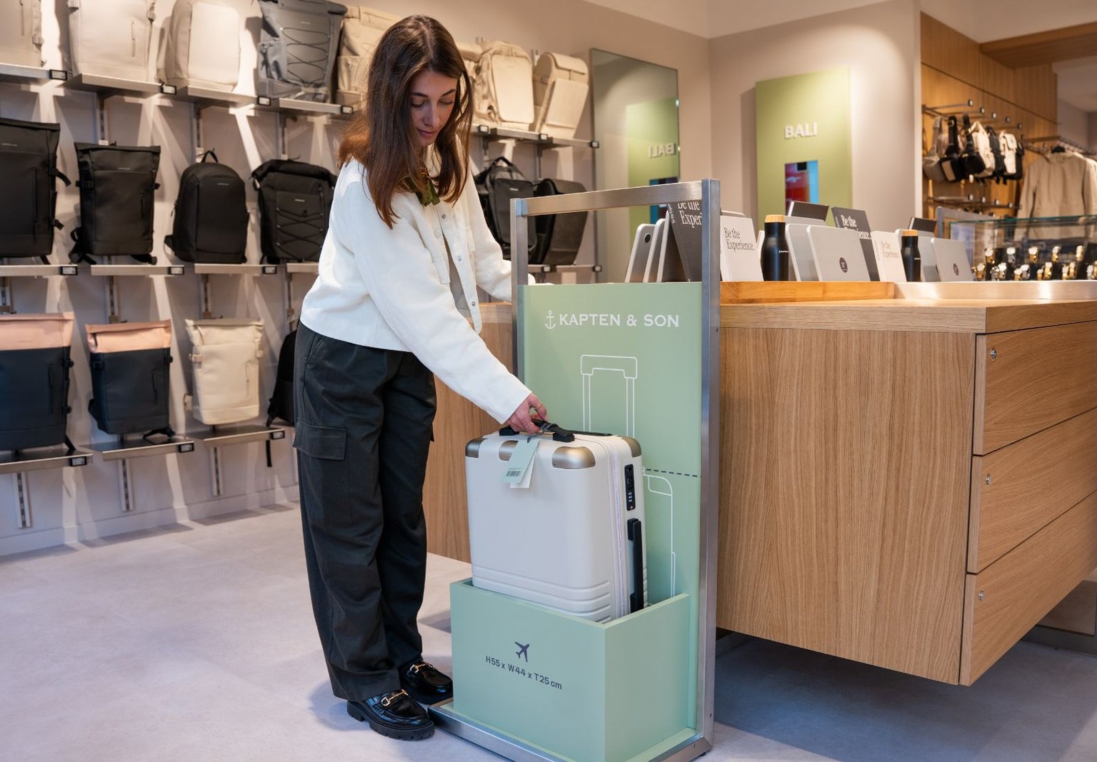 Innenansicht des Kapten & Son Experience Stores – Wandregal mit Taschen, Rucksäcken und Accessoires, Regale mit Reisegepäck und Reisetaschen sowie eine Glasvitrine mit Uhren und Schmuck