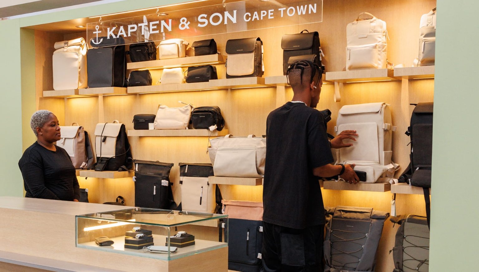 Interior of the Kapten & Son Experience Store – wall display with bags, backpacks and accessories, shelves with luggage and duffle bags, and a glass display case with watches and jewellery