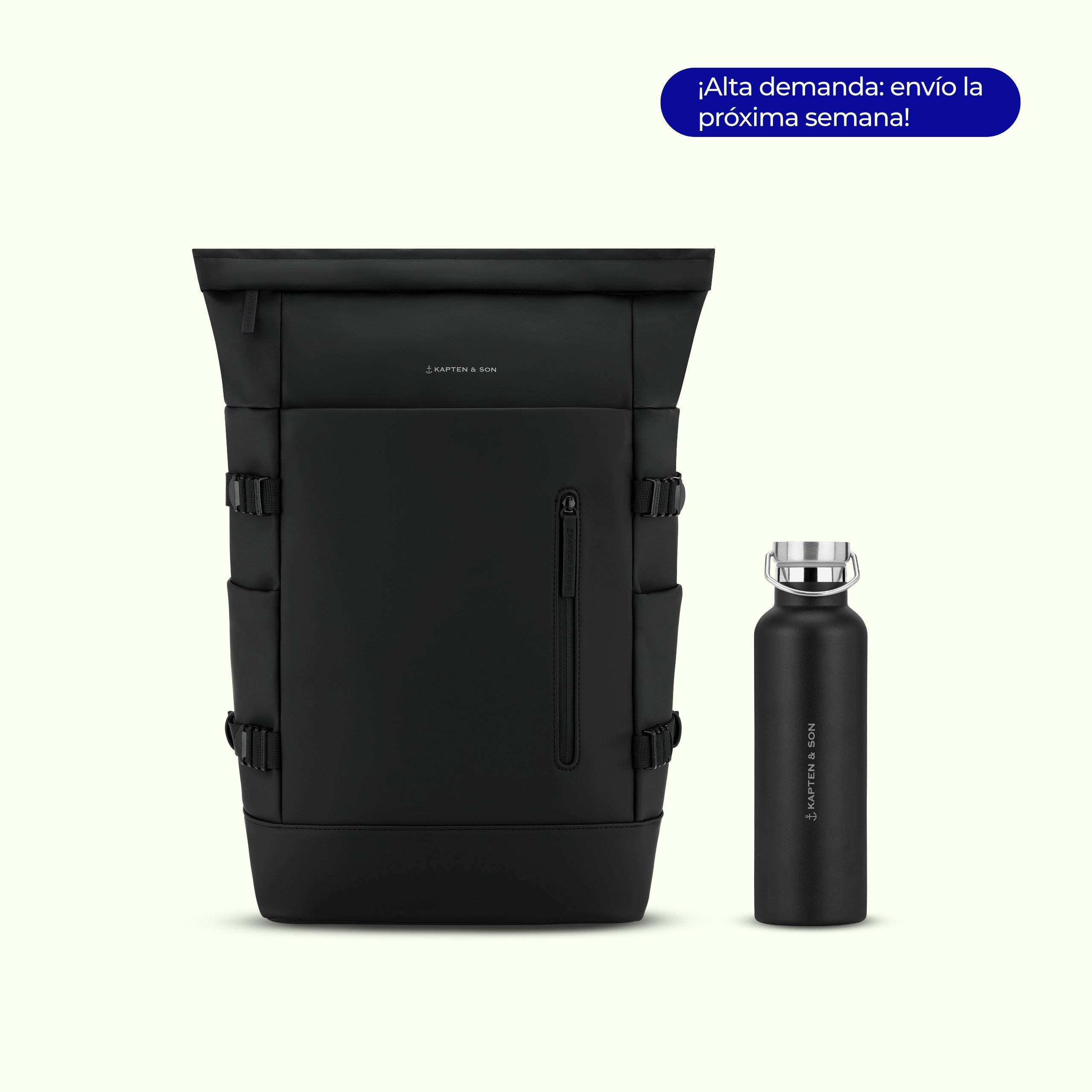 Mochila negra con cierre enrollable Helsinki de Kapten & Son con hebillas laterales y un bolsillo frontal con cremallera, junto a una botella de agua de acero inoxidable negra a juego de Kapten & Son con tapa plateada, sobre fondo claro. Un distintivo azul indica: "Debido a la alta demanda: ¡envío la próxima semana!"
