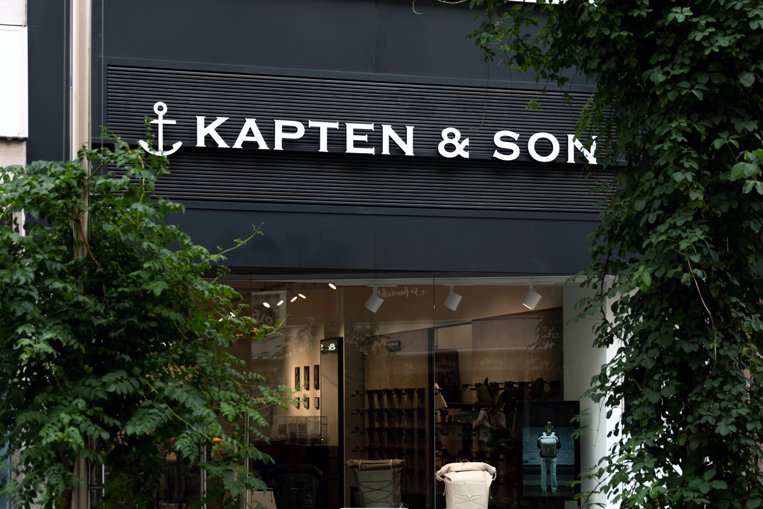 Kapten & Son Experience Store – Ladenfront mit beleuchtetem Logo, Rucksäcken, Taschen und Reisegepäck in den Schaufenstern