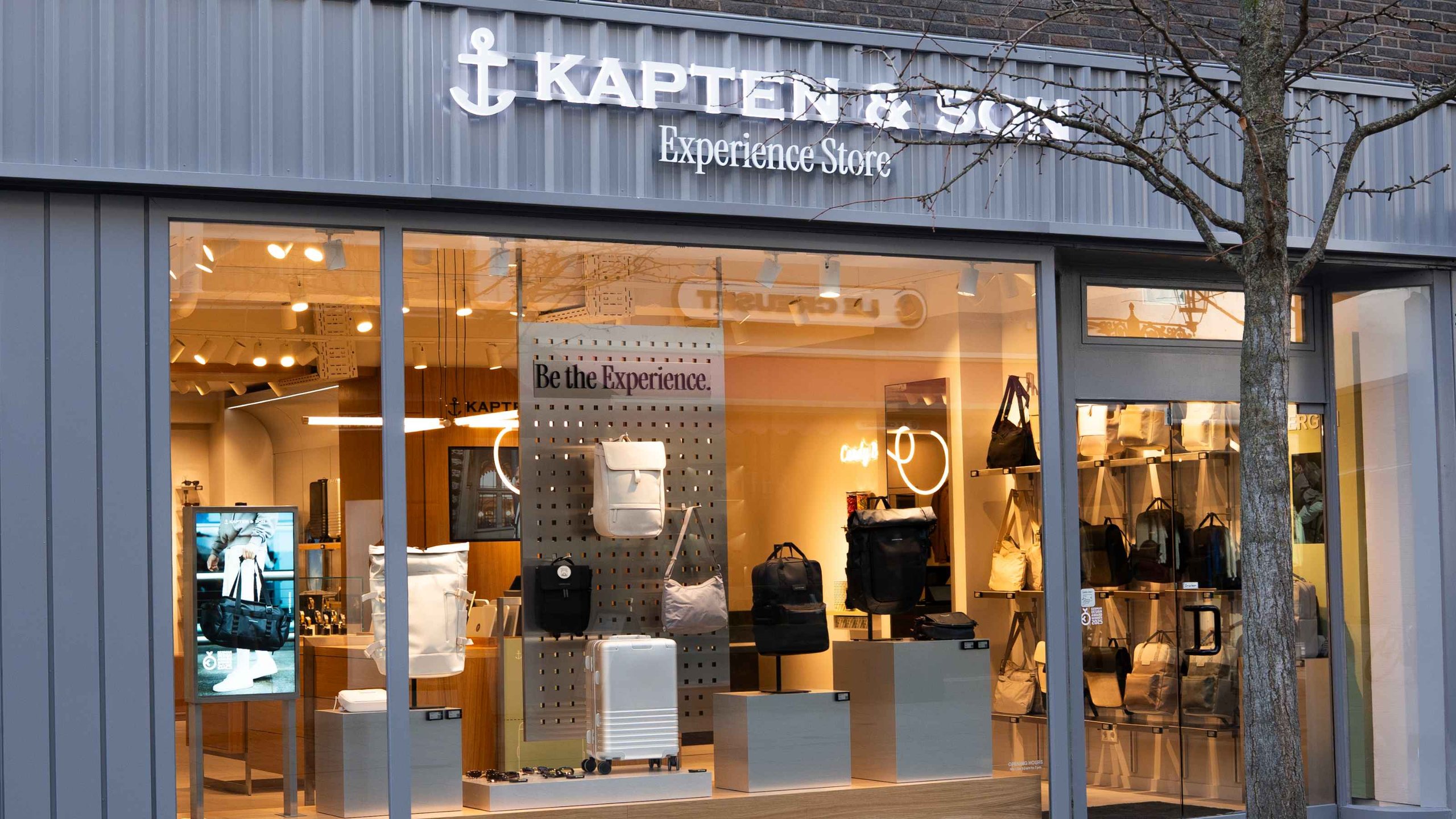 Kapten & Son Experience Store – Ladenfront mit beleuchtetem Logo, Rucksäcken, Taschen und Reisegepäck in den Schaufenstern