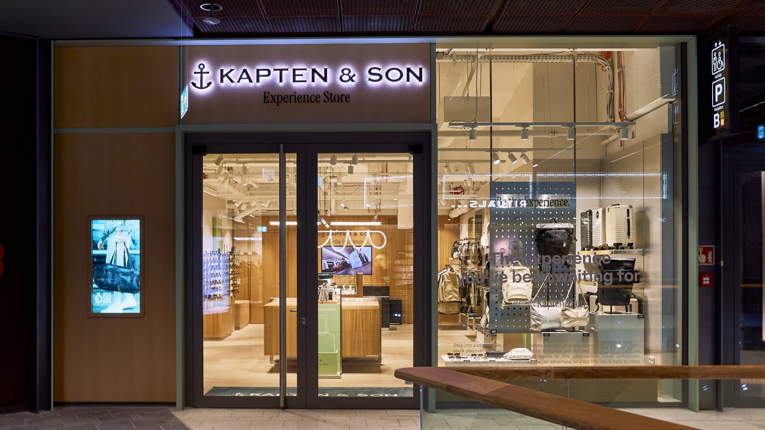 Kapten & Son Experience Store – Ladenfront mit beleuchtetem Logo, Rucksäcken, Taschen und Reisegepäck in den Schaufenstern