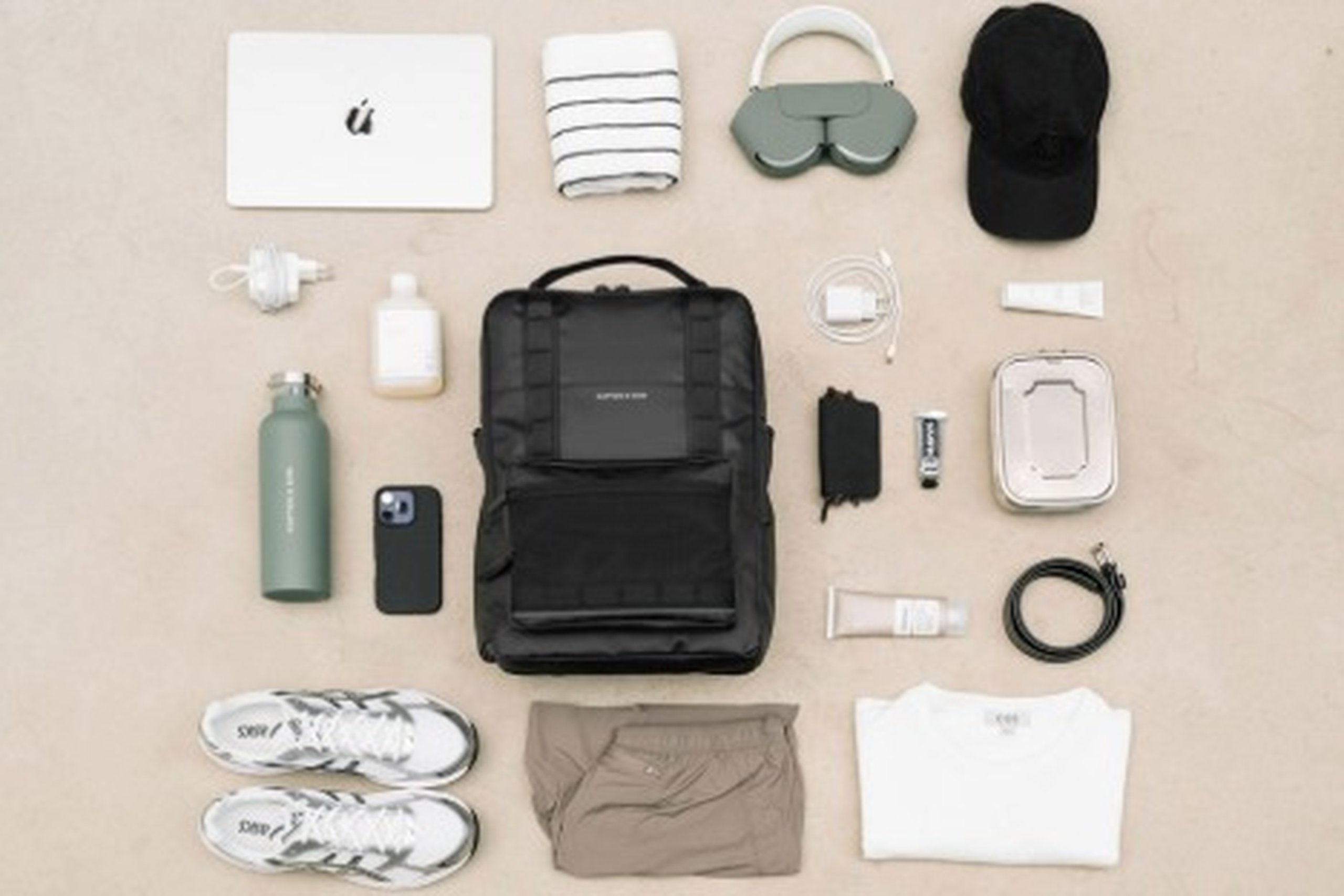 ausgebreitete essentials wie laptop, kopfhörer, schuhe neben einem rucksack