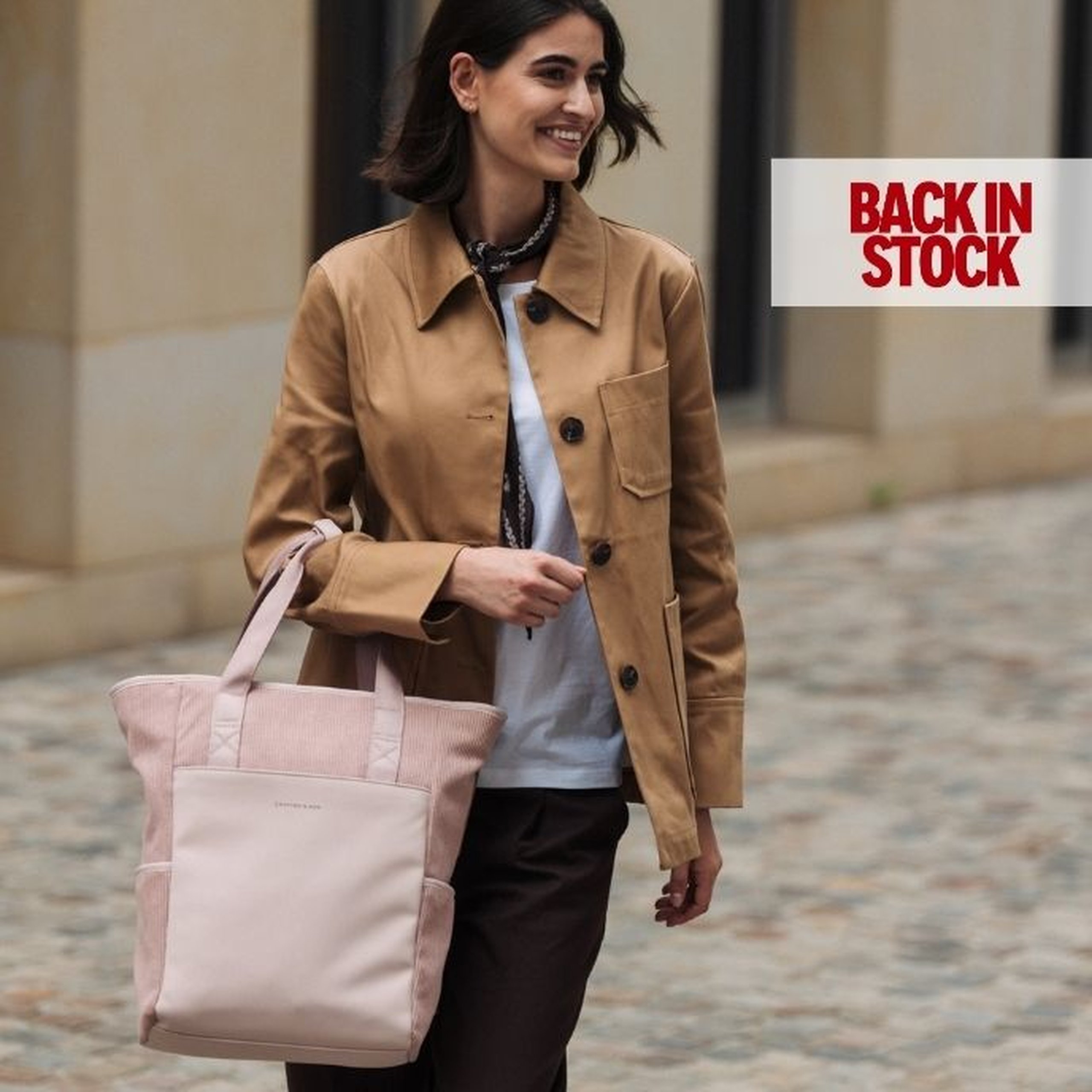 Mujer sonriente con un bolso tote Lindby rosa en un entorno urbano; mensaje « Back in Stock ».