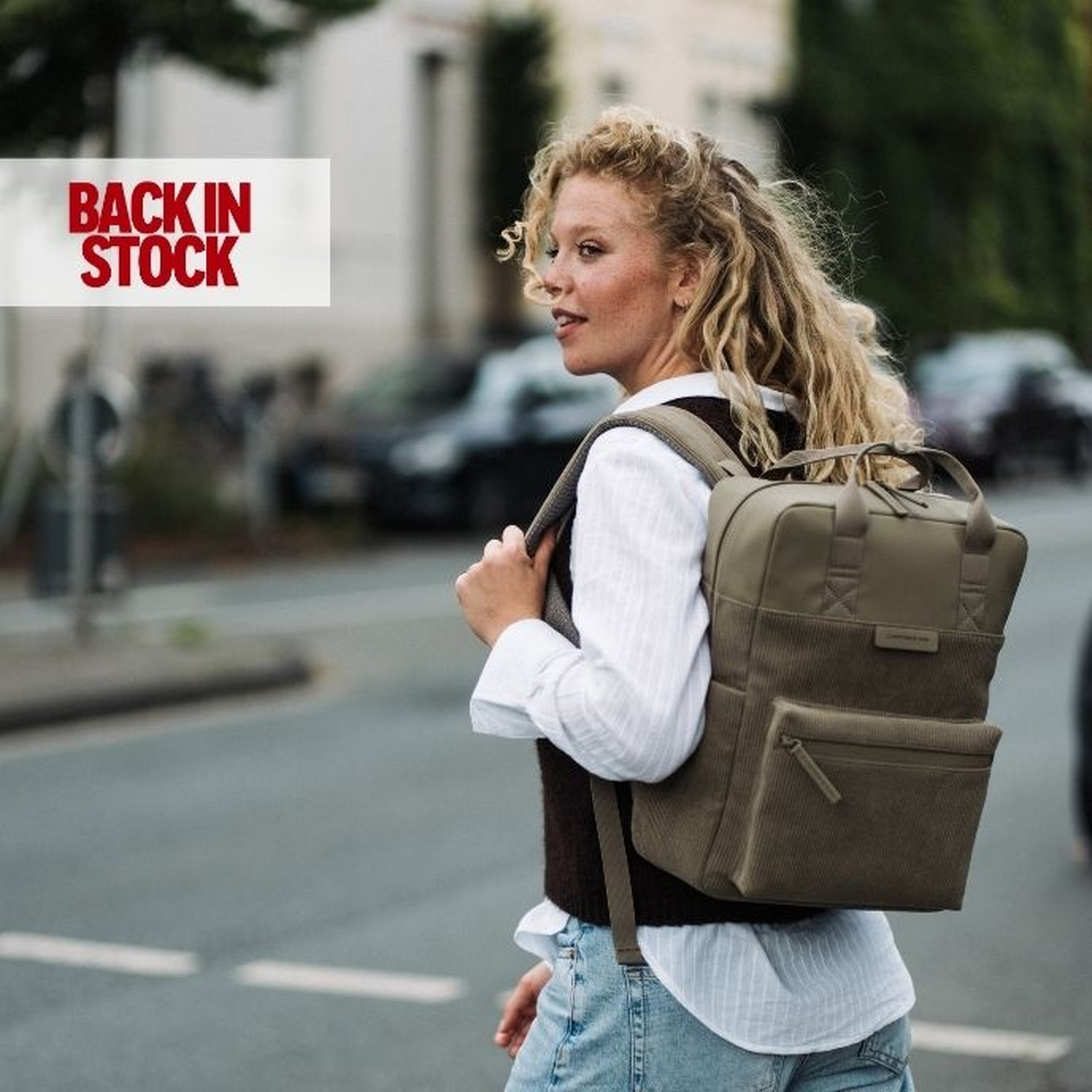Mujer con una mochila Bergen verde oliva en un entorno urbano; mensaje « Back in Stock ».