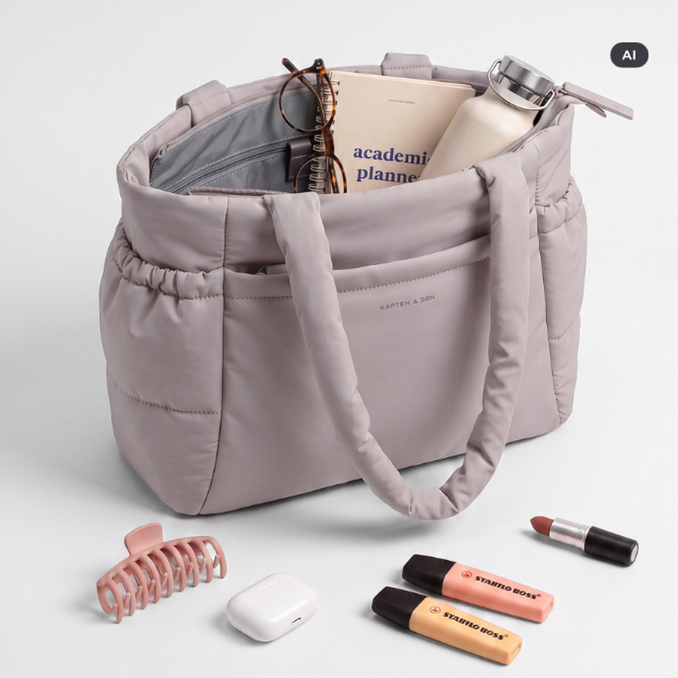 AI Generated Image: Eine hellviolette gesteppte Kapten & Son Tote Bag, geöffnet mit sichtbarem Inhalt wie Planer, Brille und Trinkflasche, daneben Accessoires wie Haarklammer, AirPods, Lippenstift und Stabilo-Marker.