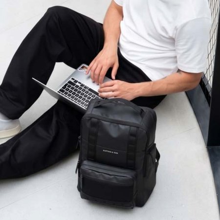 junger mann tippt auf laptop und hat seinen kapten son laptoprucksack neben sich liegen