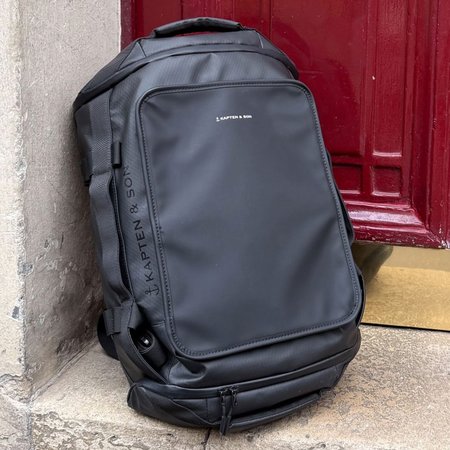 Zwarte duffle bag leunt tegen een deur