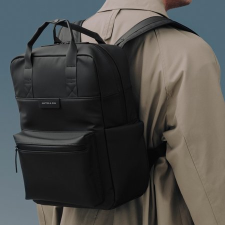 junger man am strand trägt beigen rolltoprucksack von kapten & son
