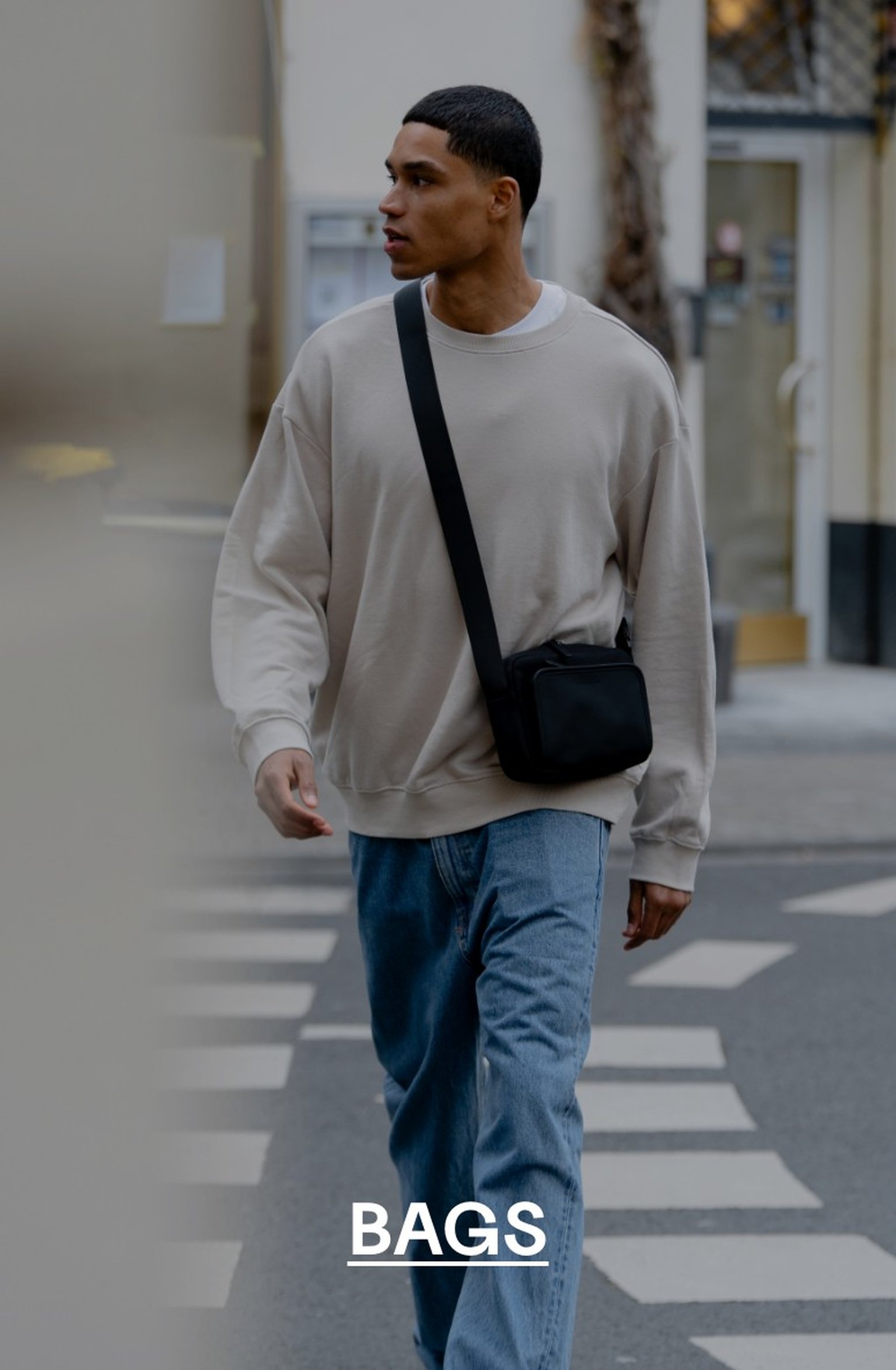 Man walking across a zebra crossing in a beige sweatshirt and jeans, wearing a black Kapten & Son crossbody bag – text overlay: "BAGS"