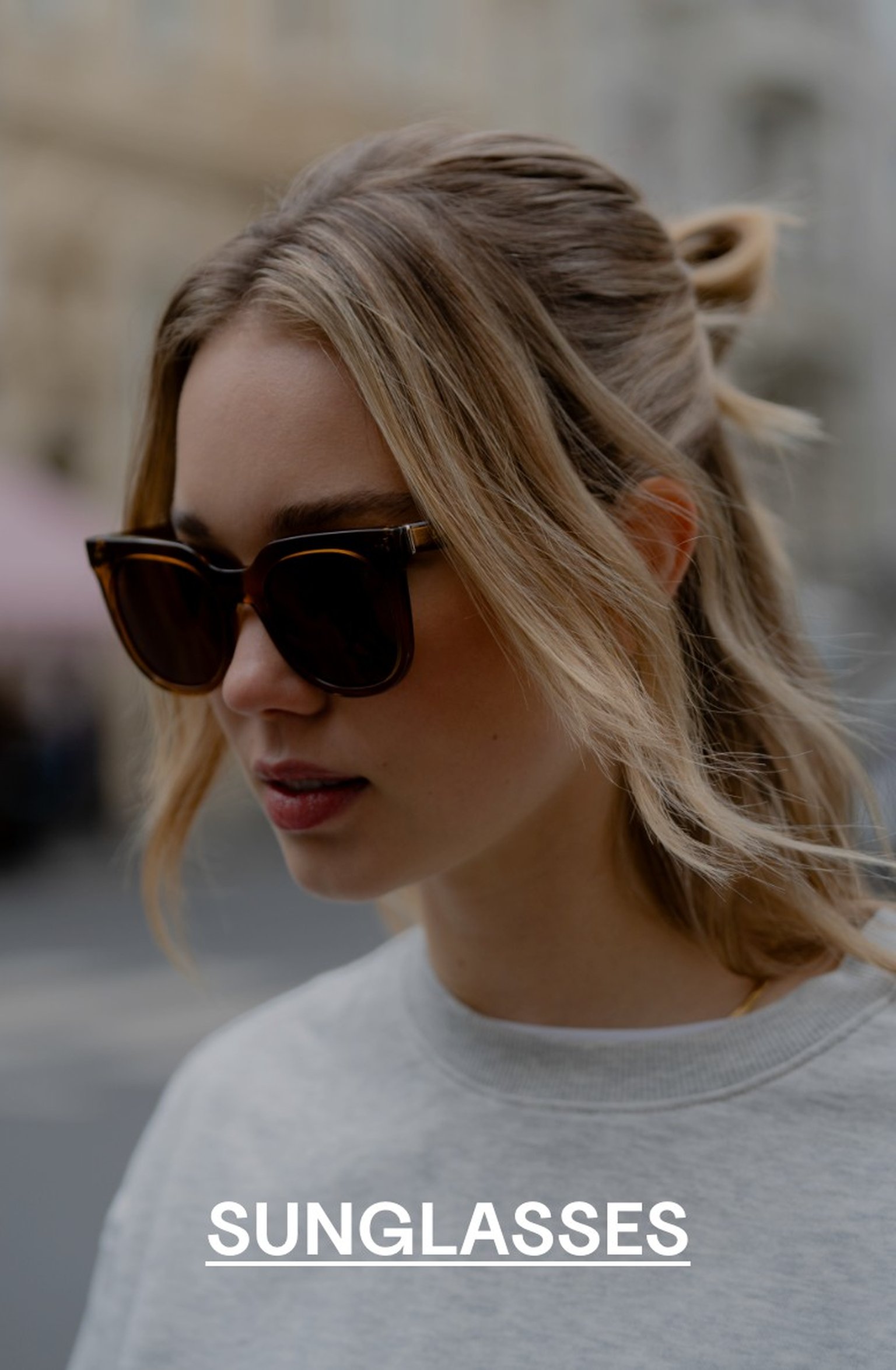 Woman with blonde hair wearing tortoiseshell Kapten & Son sunglasses and a light grey sweatshirt, looking down – text overlay: "SUNGLASSES"