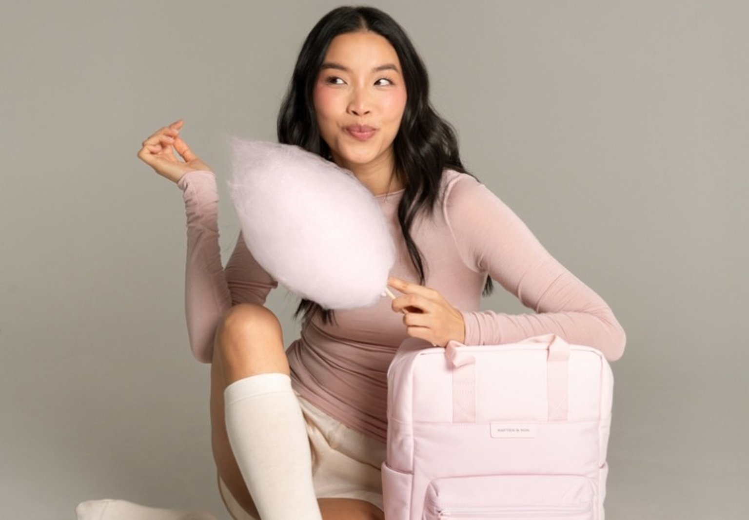 junge frau stützt sich auf pastellfarbenen rucksack ab und isst zuckerwatte