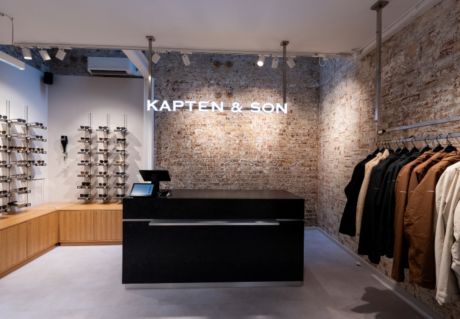 Innenansicht des Kapten & Son Experience Stores – Wandregal mit Taschen, Rucksäcken und Accessoires, Regale mit Reisegepäck und Reisetaschen sowie eine Glasvitrine mit Uhren und Schmuck