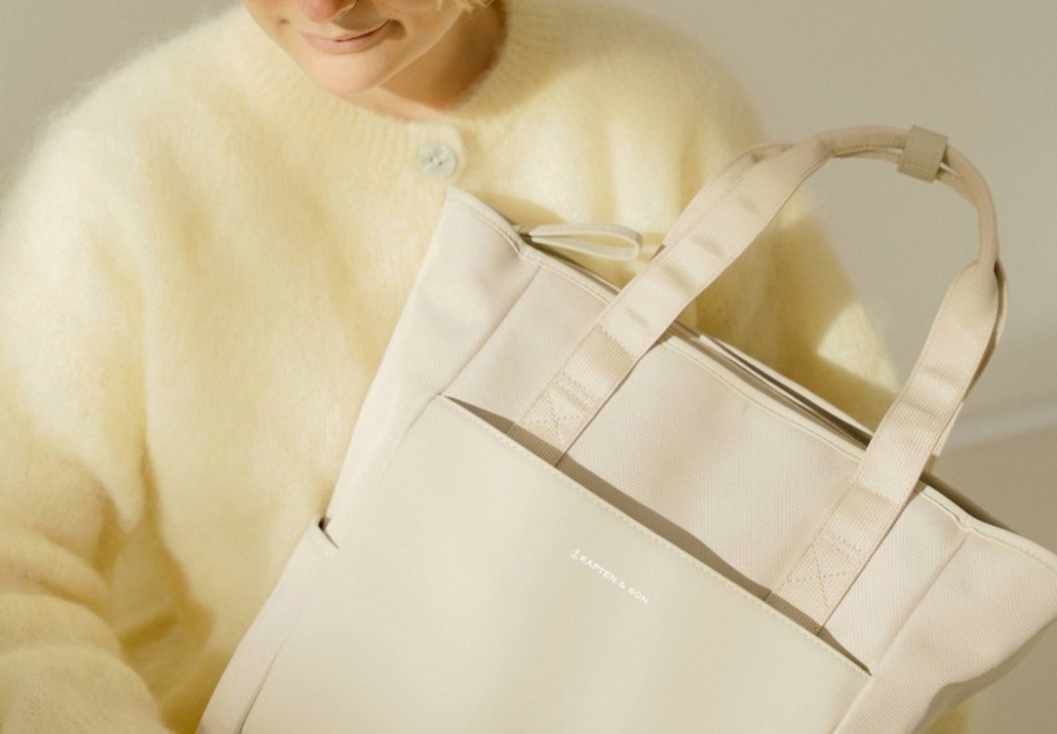 junge frau hält einen kapten and son wickelrucksack in beige