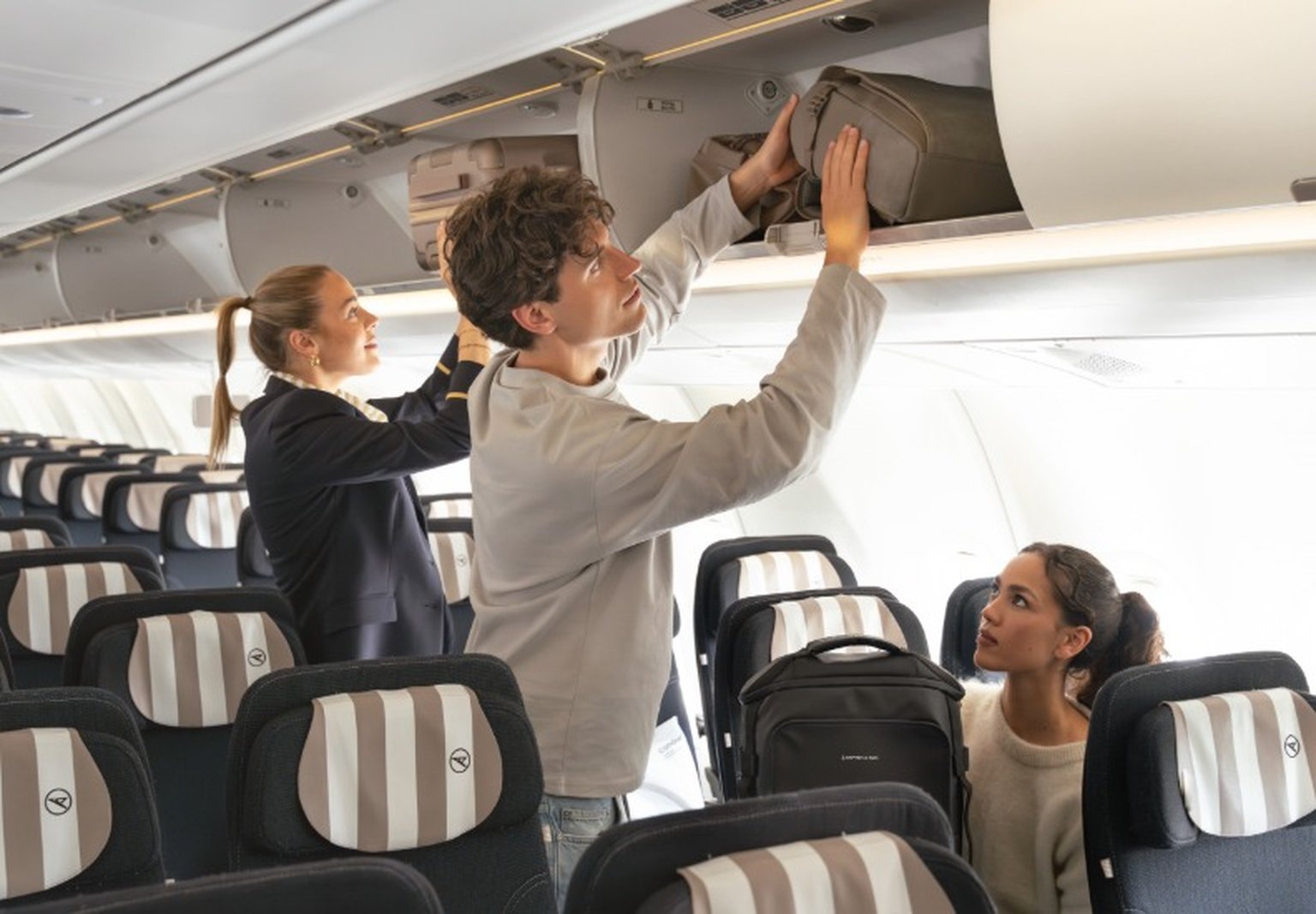 junger mann schiebt kapten son rucksack ins handgepäckfach im flieger