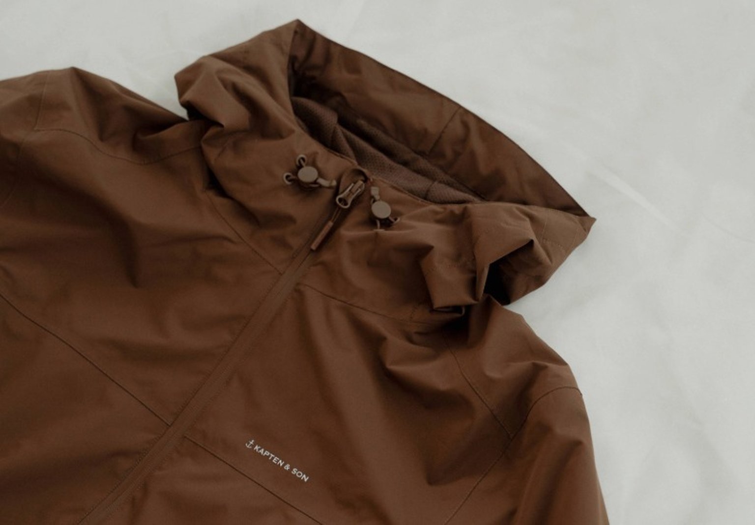 braune regenjacke von kapten and son auf weißem untergrund