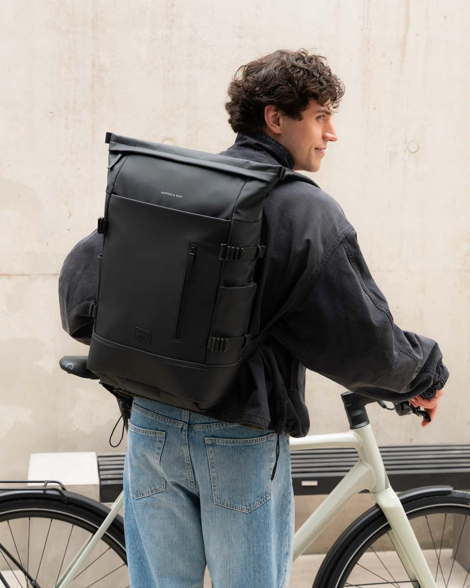 junger mann schiebt sein fahrrad und trägt einen commuter rucksack von kapten son