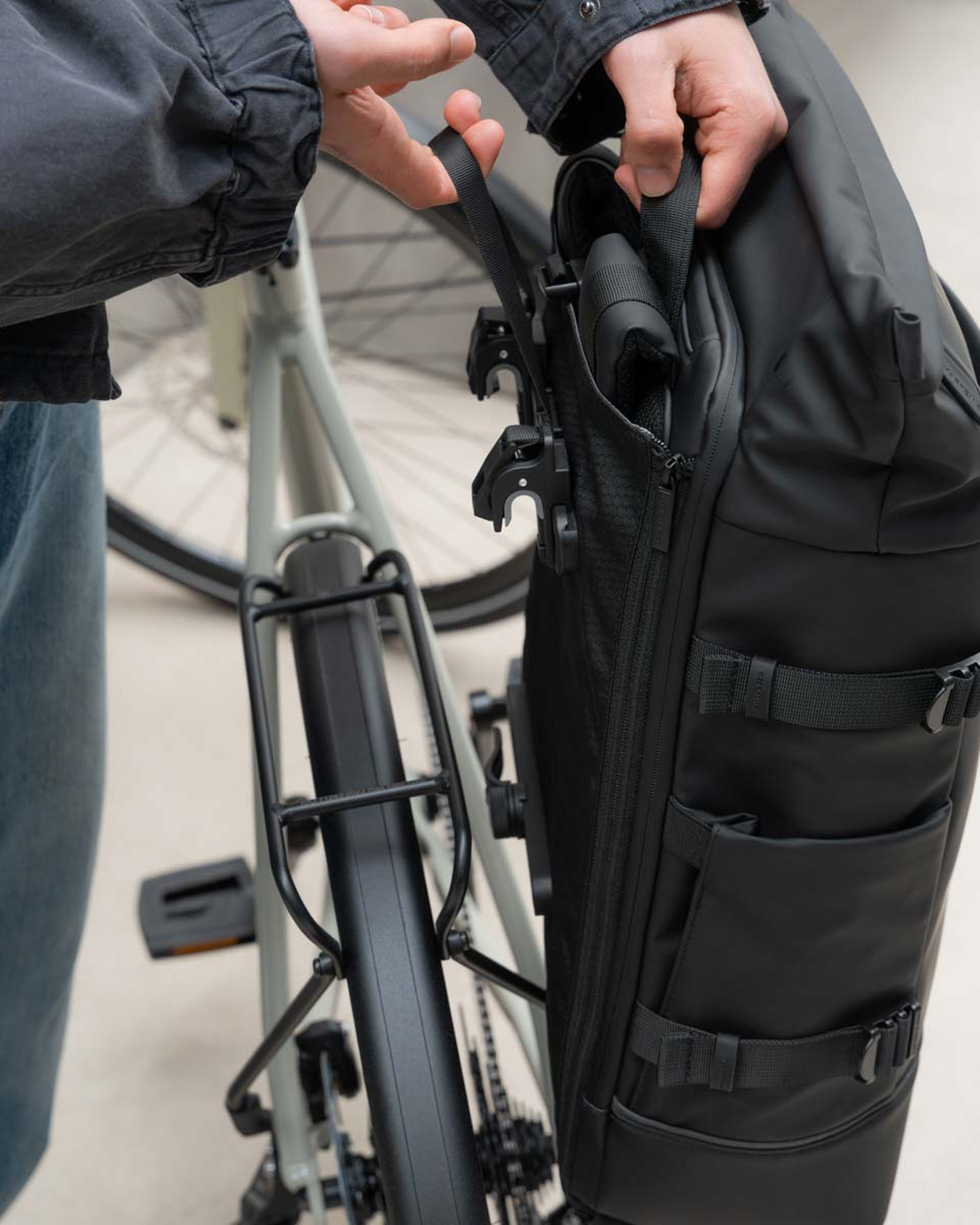 Eine Person befestigt eine schicke, schwarze Tasche am Gepäckträger eines Fahrrads. Die Szene vermittelt Aufbruchstimmung und einen aktiven Lebensstil. Der Fokus liegt auf den Händen und der Tasche.