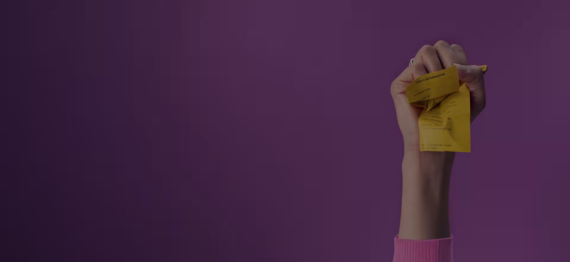A hand in a pink sleeve holds a crumpled yellow paper against a purple background.