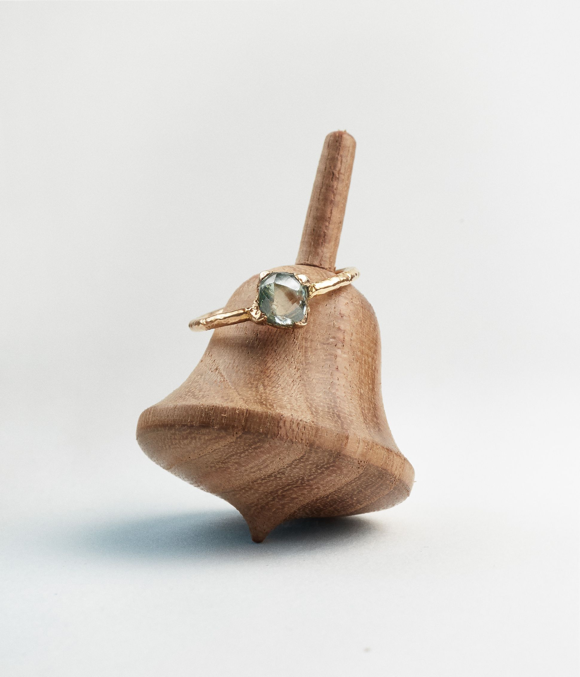 Bague en or jaune recyclé 18k avec pierre verte facettée, posée sur un support en bois sculpté.