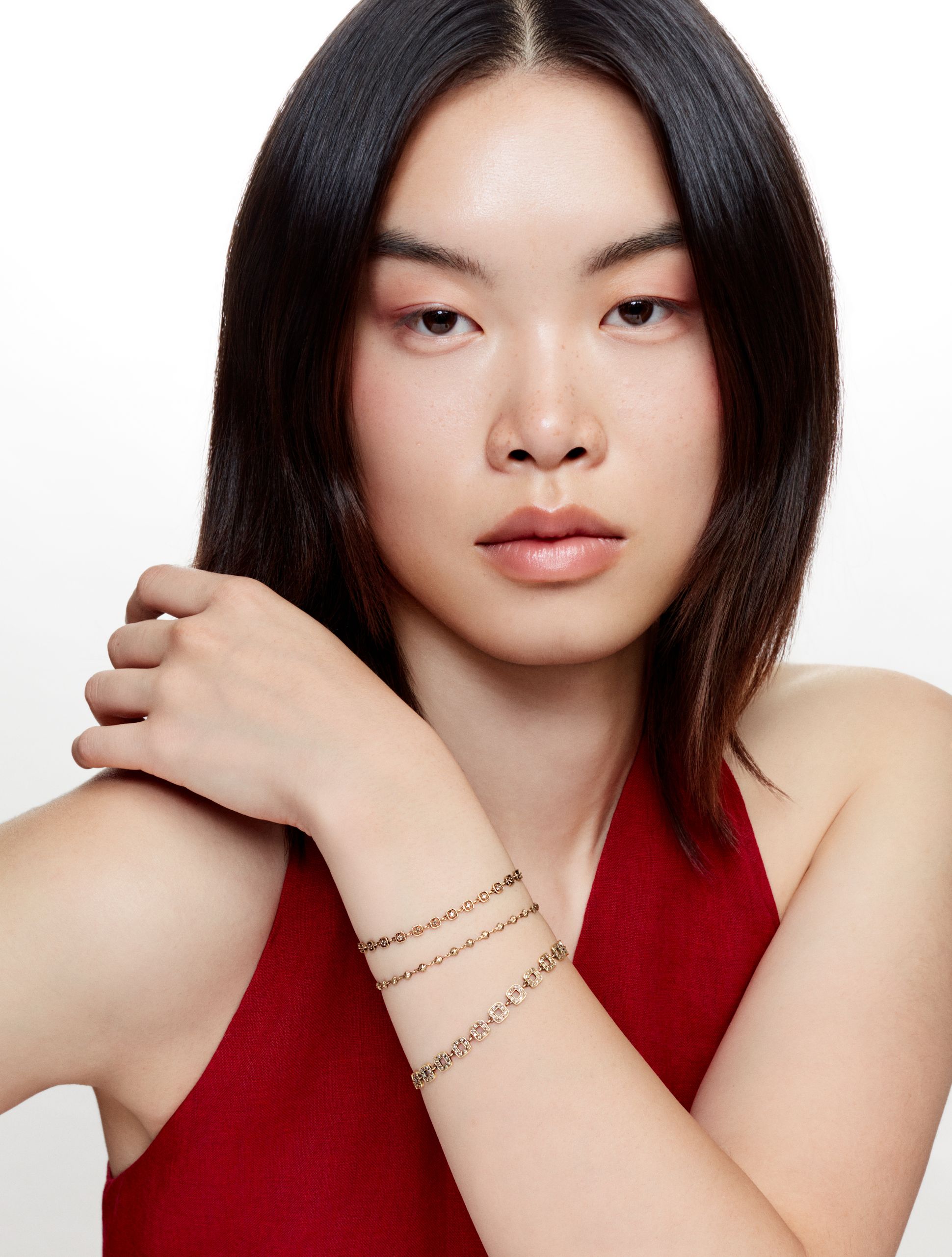 Femme portant trois bracelets fins en or jaune sur son poignet, posant en top rouge sur fond blanc.